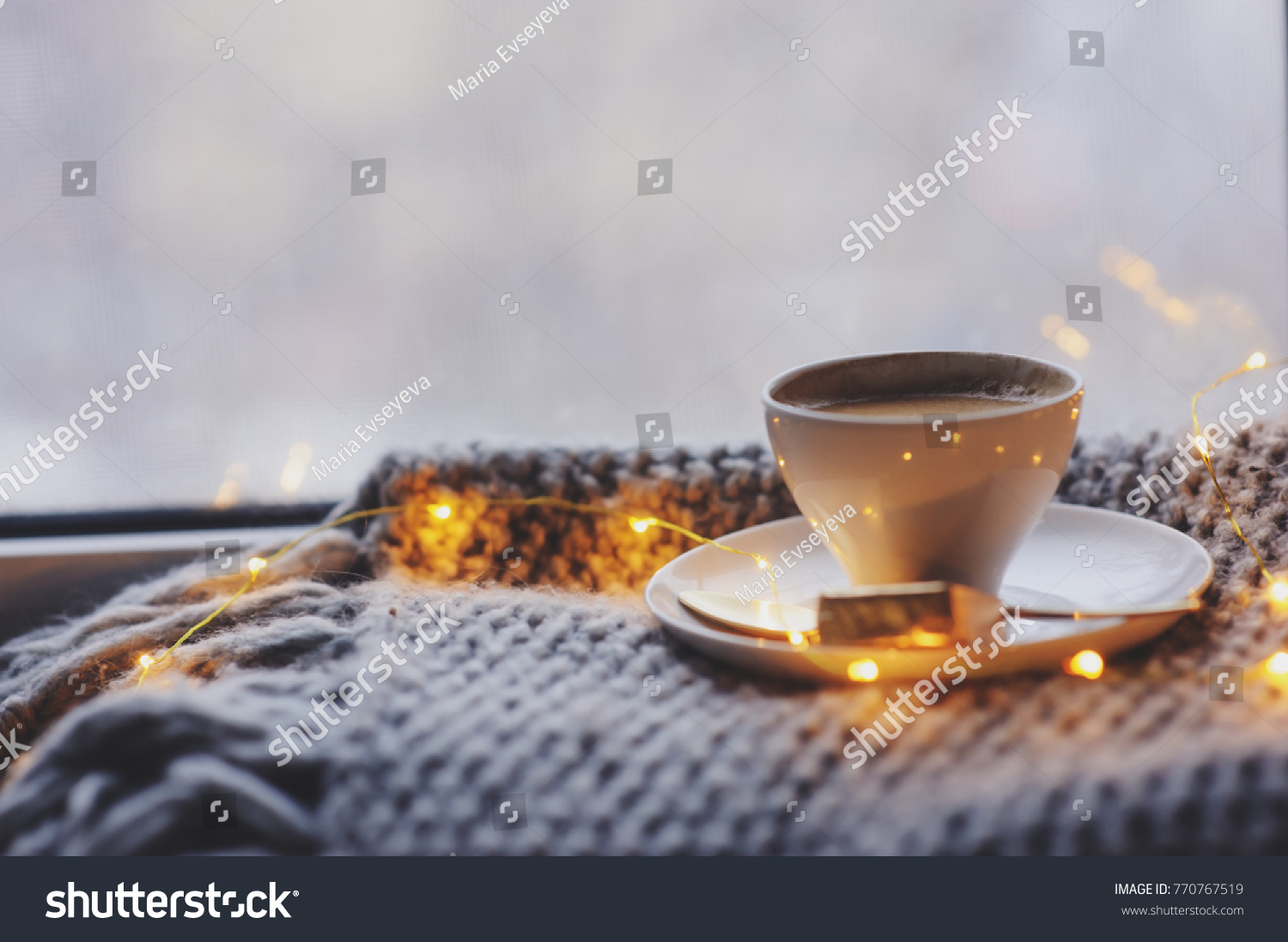 cozy winter or autumn morning at home. Hot coffee with gold metallic spoon, warm blanket, garland and candle lights, swedish hygge concept. #770767519