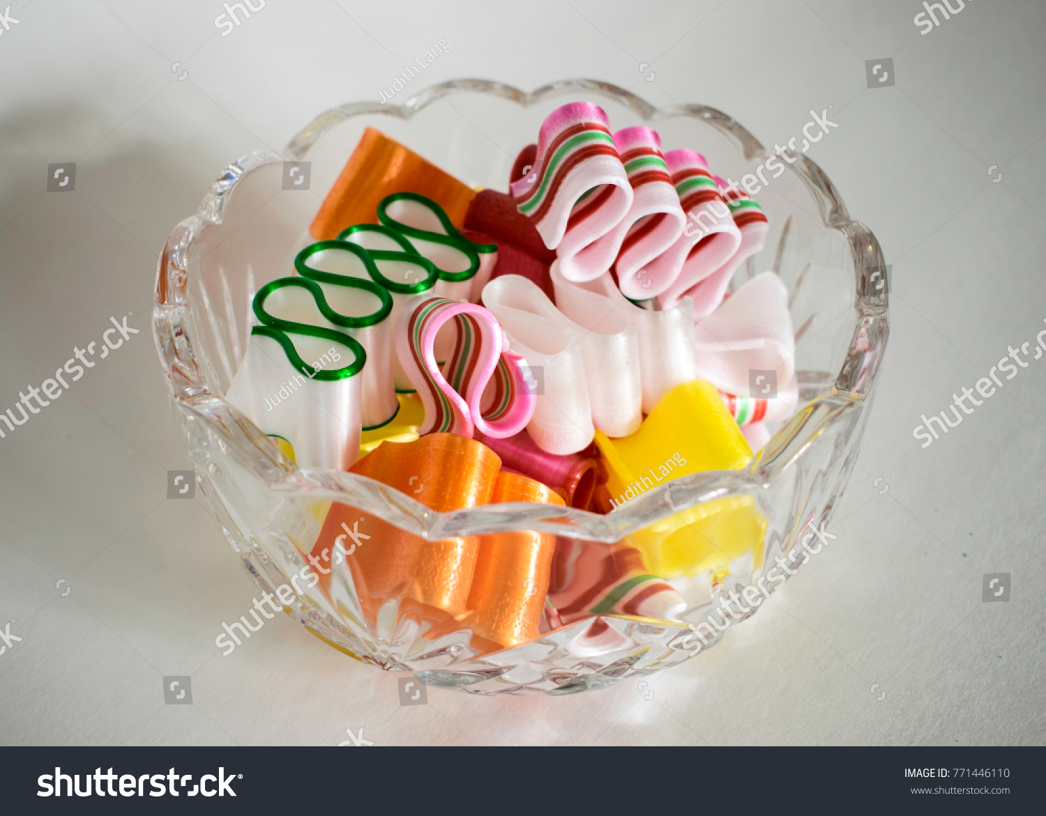 Beautiful crystal bowl is filled with colorful curving ribbon candy on white background. #771446110