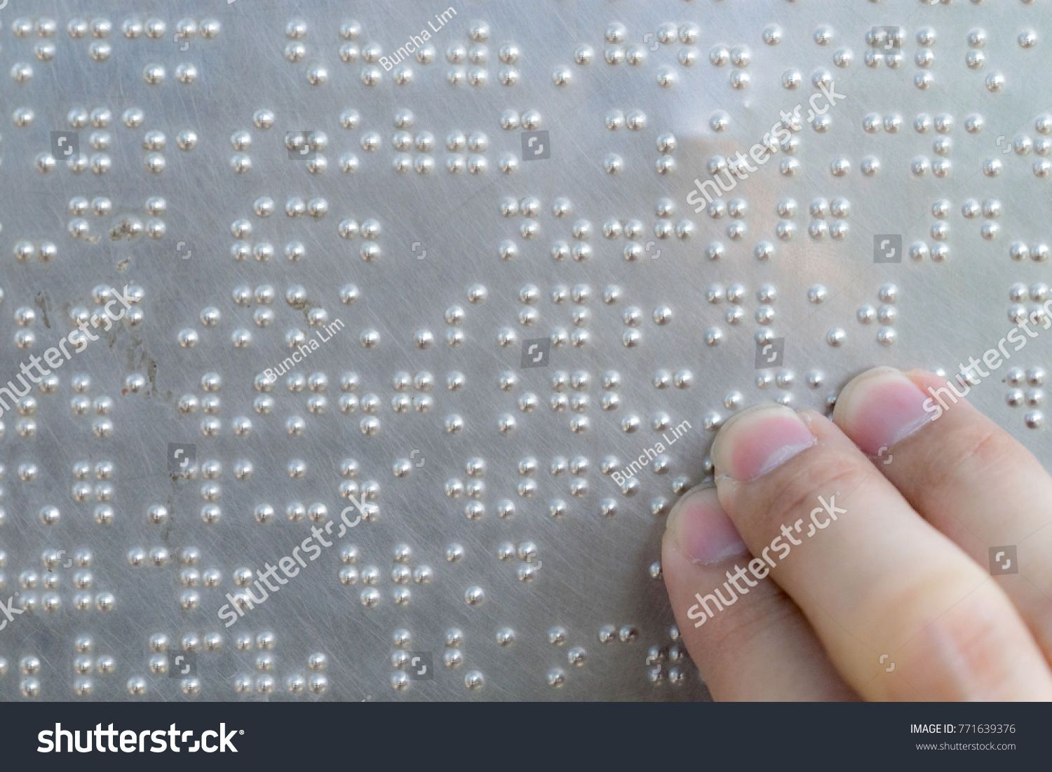 Fingers on the metal plate written in the Braille letters #771639376