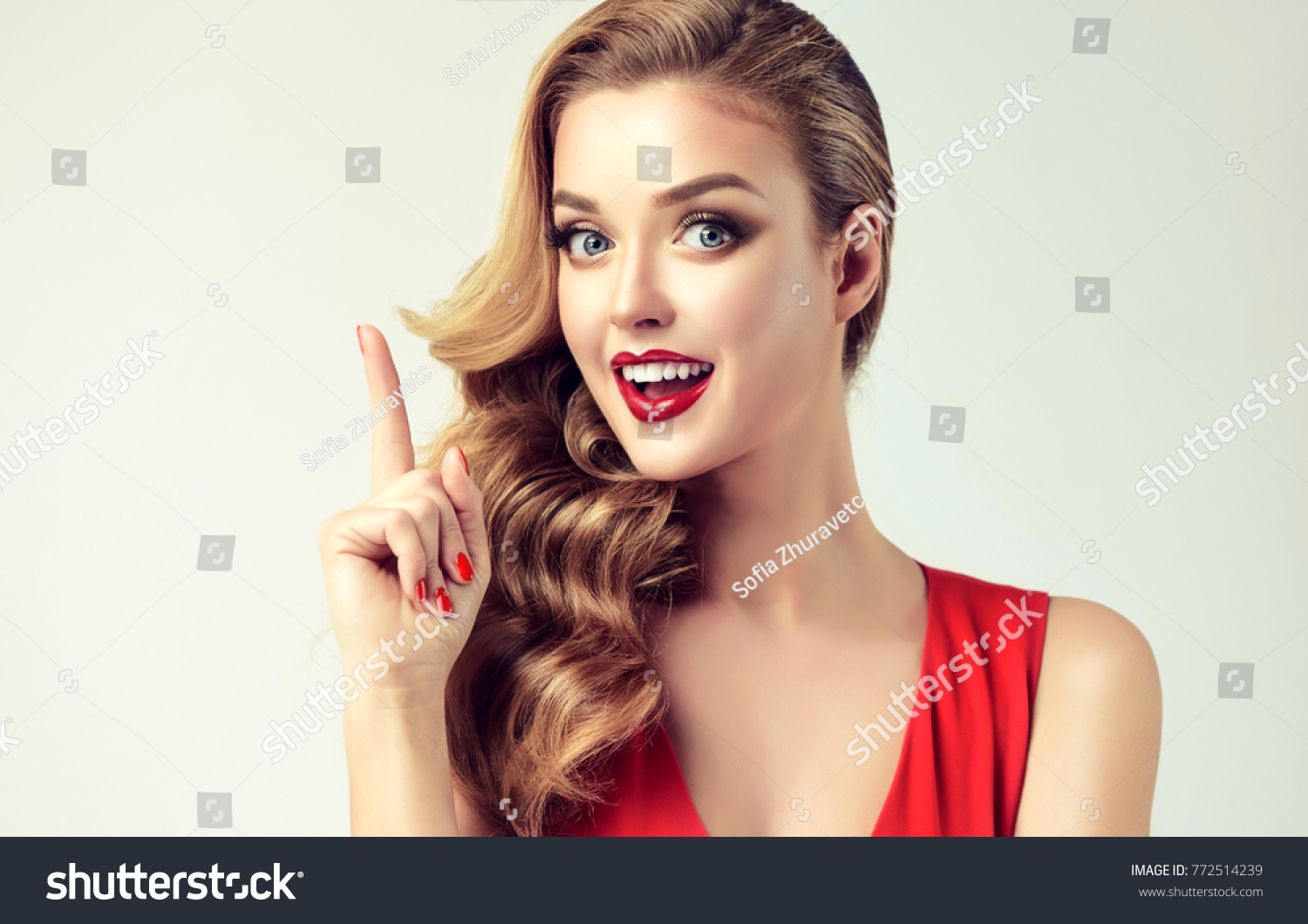 Surprised woman showing product .Beautiful girl with curly hair, pointing a finger at the top . Presenting your product. Expressive facial expressions . Teaching and edification . #772514239