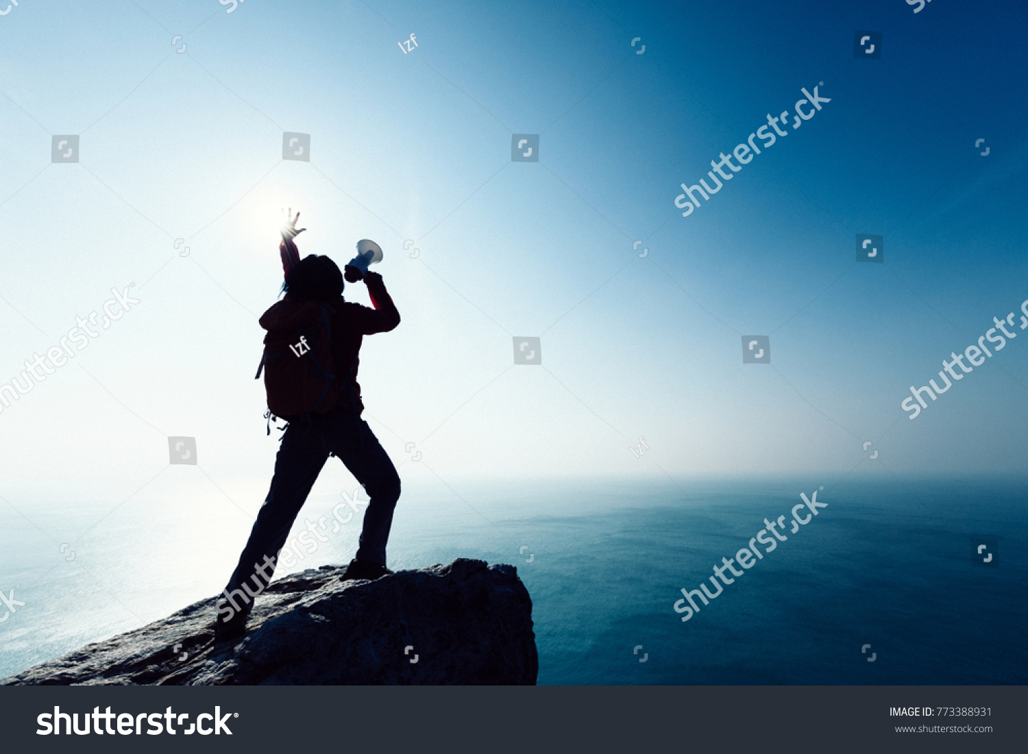 female shouting with loudspeaker on windy sunrise coast cliff edge #773388931