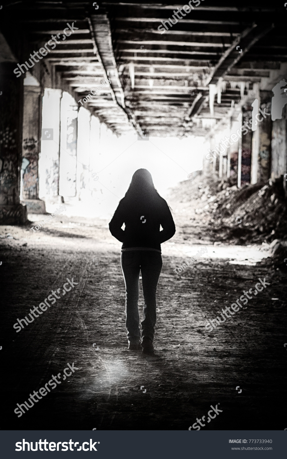 Light at the end of the tunnel.  A  silhouette of a woman walks out of an abandoned subway tunnel walking toward the light. #773733940