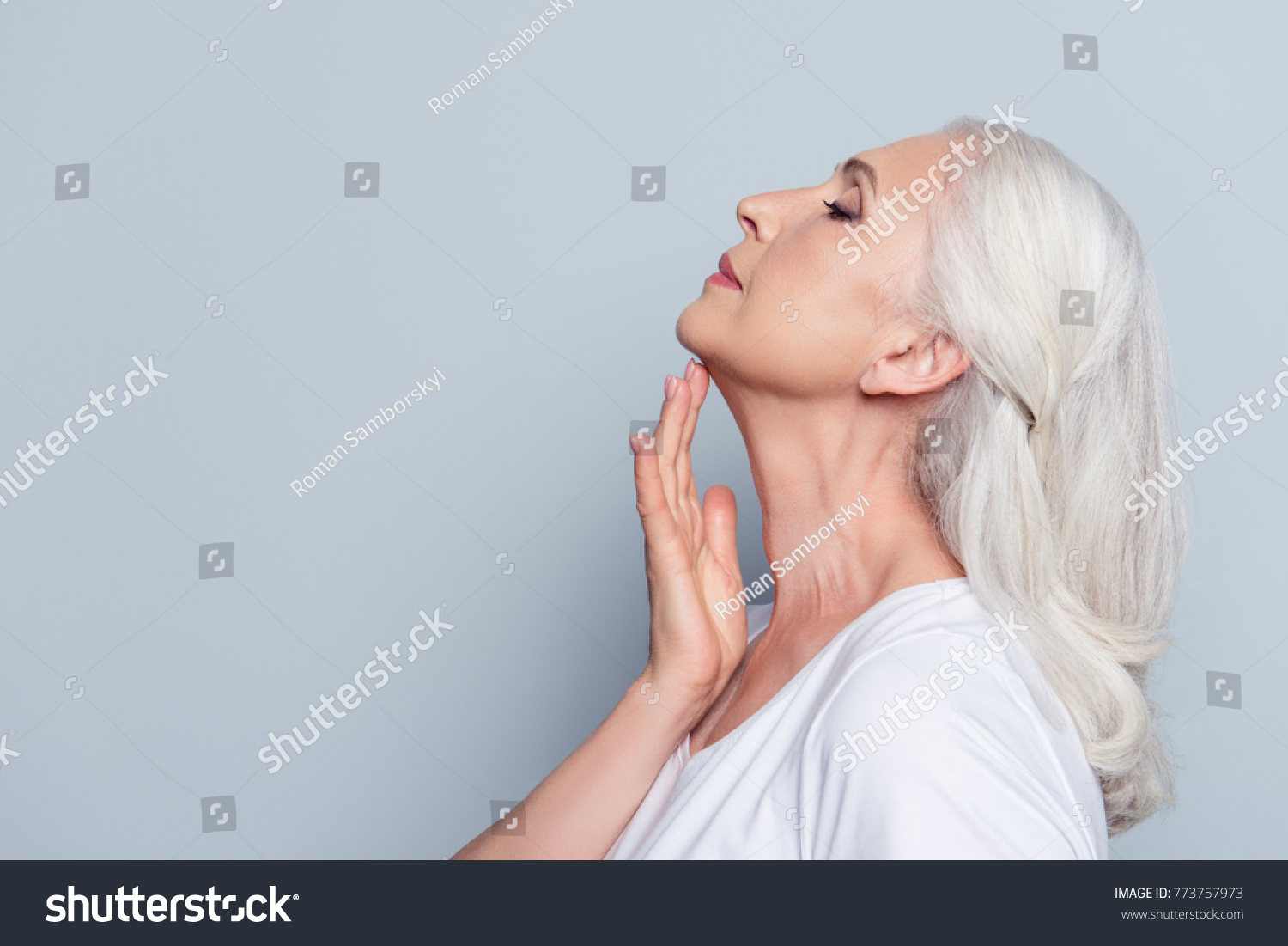 Advertisement concept. Close up profile with copy space of nice, charming, aged woman, touching her skin of neck with hand over grey background #773757973