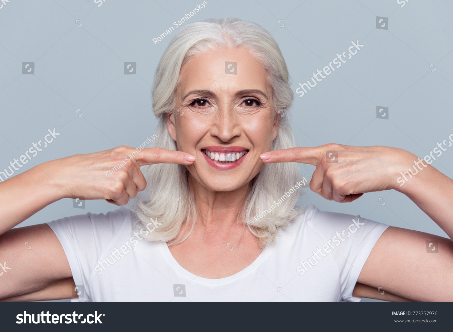 Concept of having strong healthy straight white teeth at old age. Close up portrait of happy with beaming smile female pensioner pointing on her perfect clear white teeth, isolated on gray background #773757976