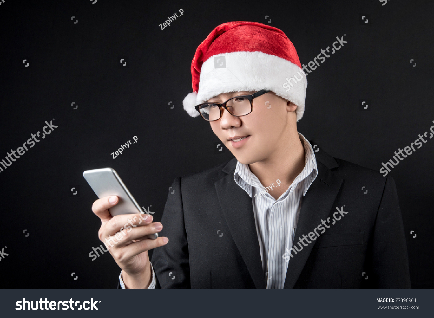 Young Asian businessman wearing suit and santa hat using smartphone on black background, male entrepreneur in christmas holiday and new year party concepts #773969641