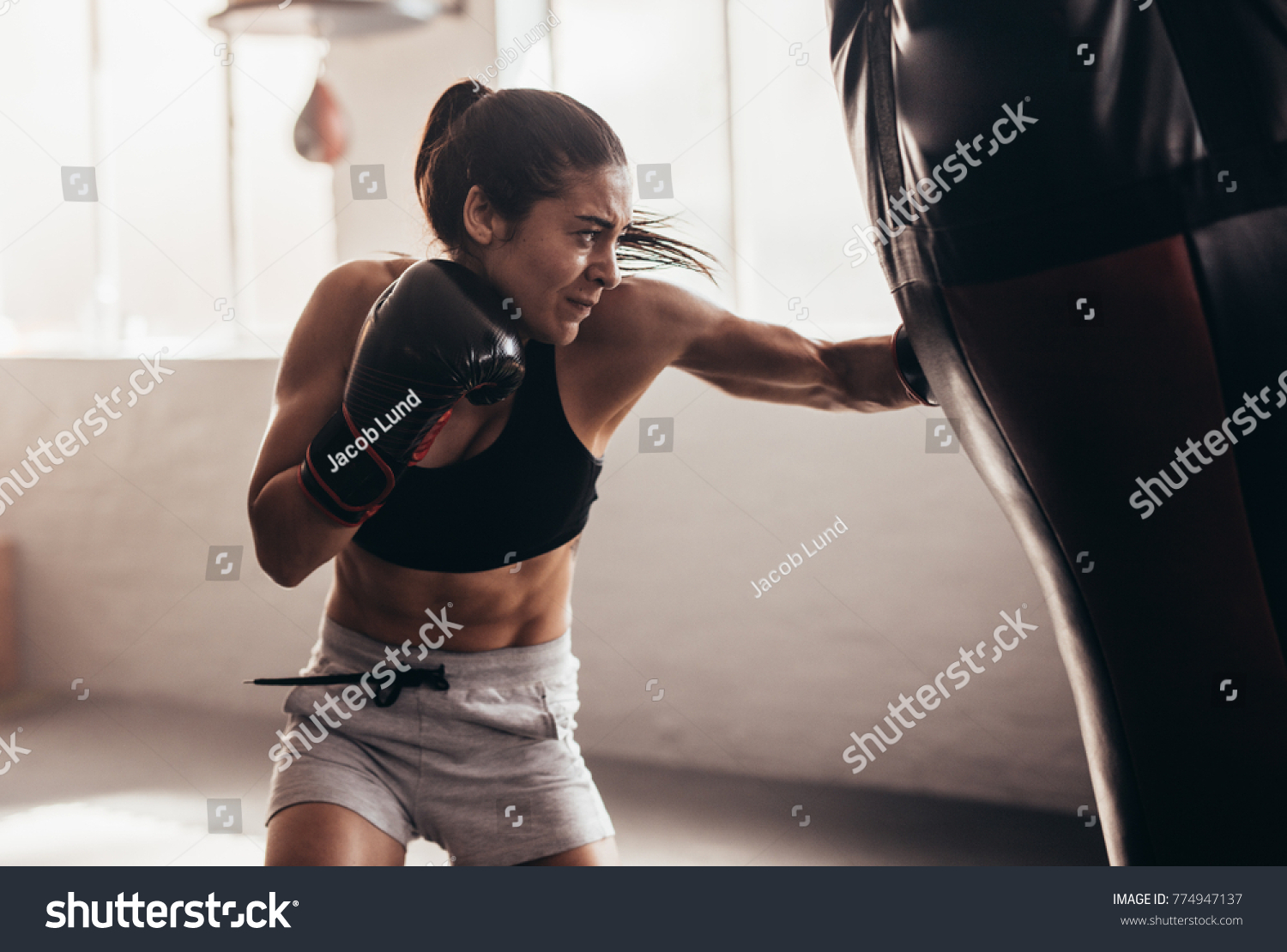 Female boxer hitting a huge punching bag at a boxing studio. Woman boxer training hard. #774947137