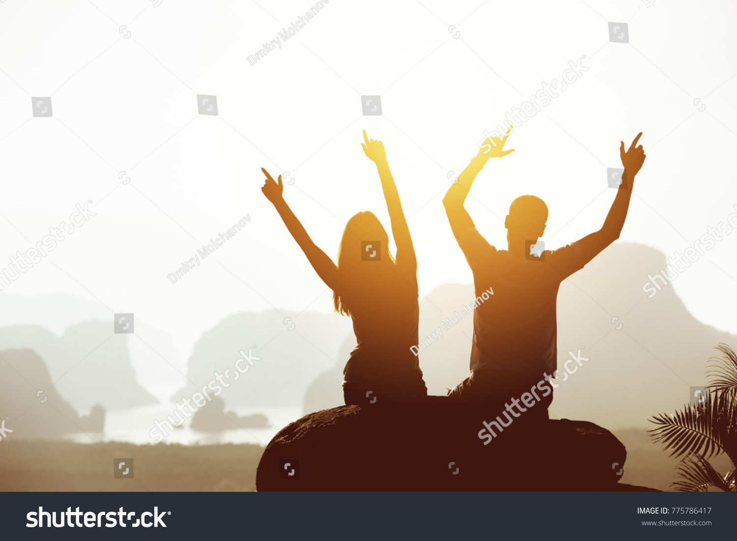 Travel concept with happy couple sitting on big rock with raised arms on mountains and islands backdrop. Place for text #775786417