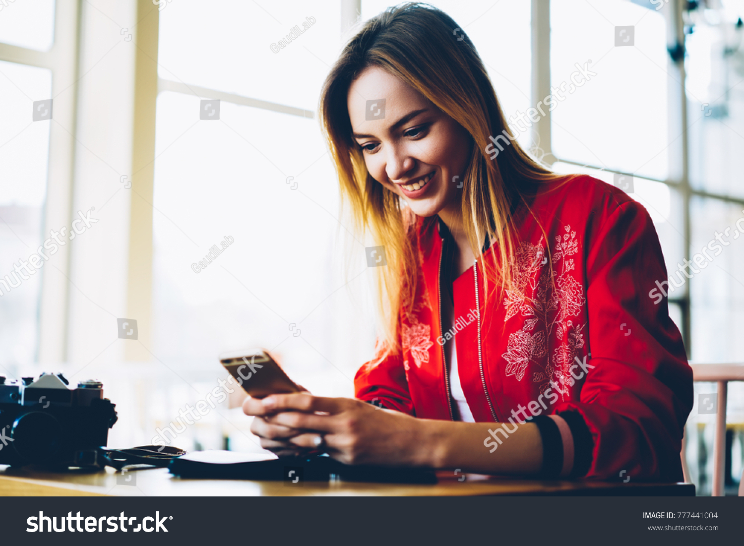 Happy young professional photographer installing new photo application on modern telephone device.Positive female blogger uploading pictures and videos on own web page via high speed internet #777441004