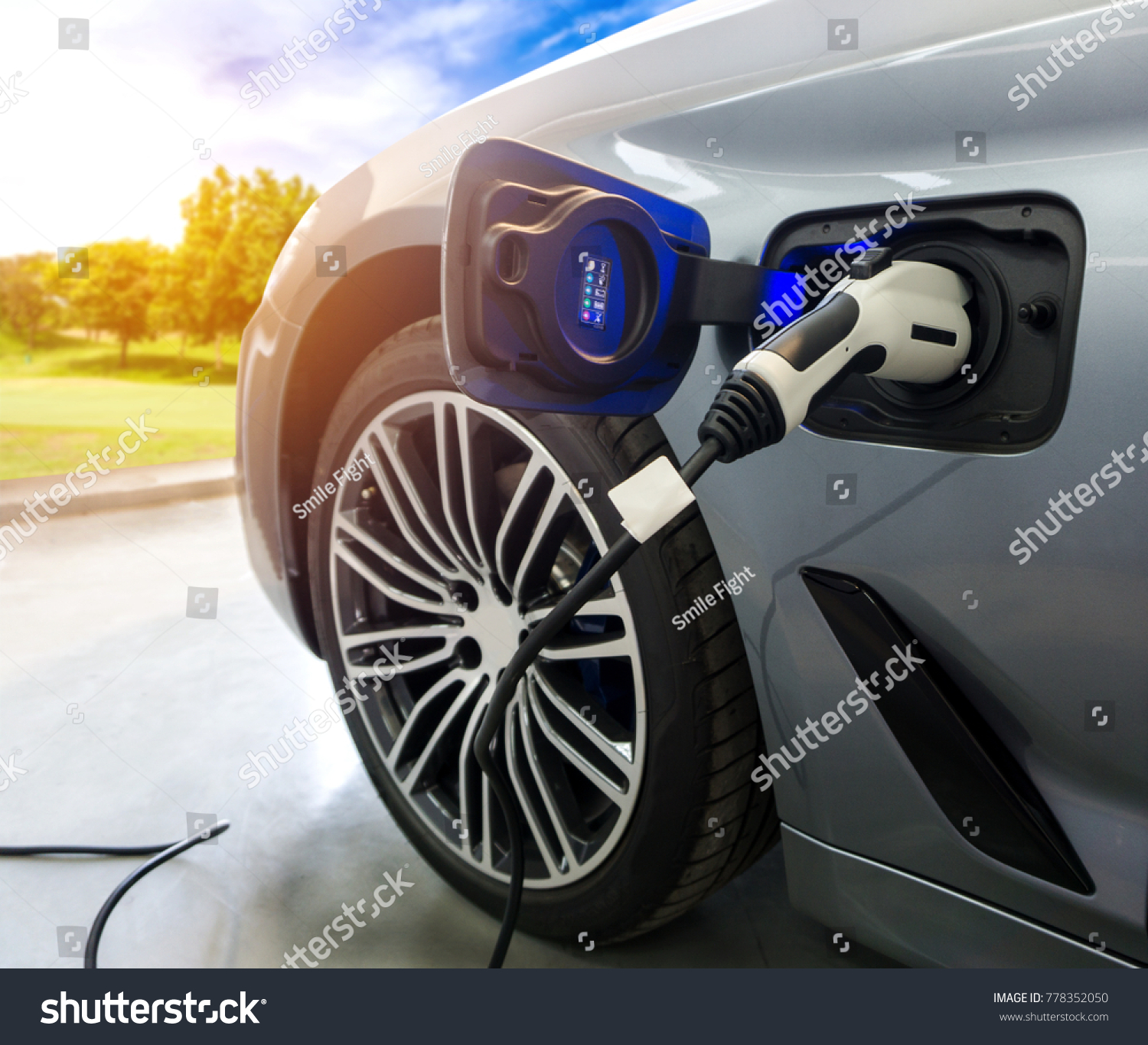 EV Car or Electric car at charging station with the power cable supply plugged in on blurred nature with sun light background. Eco-friendly alternative energy concept #778352050