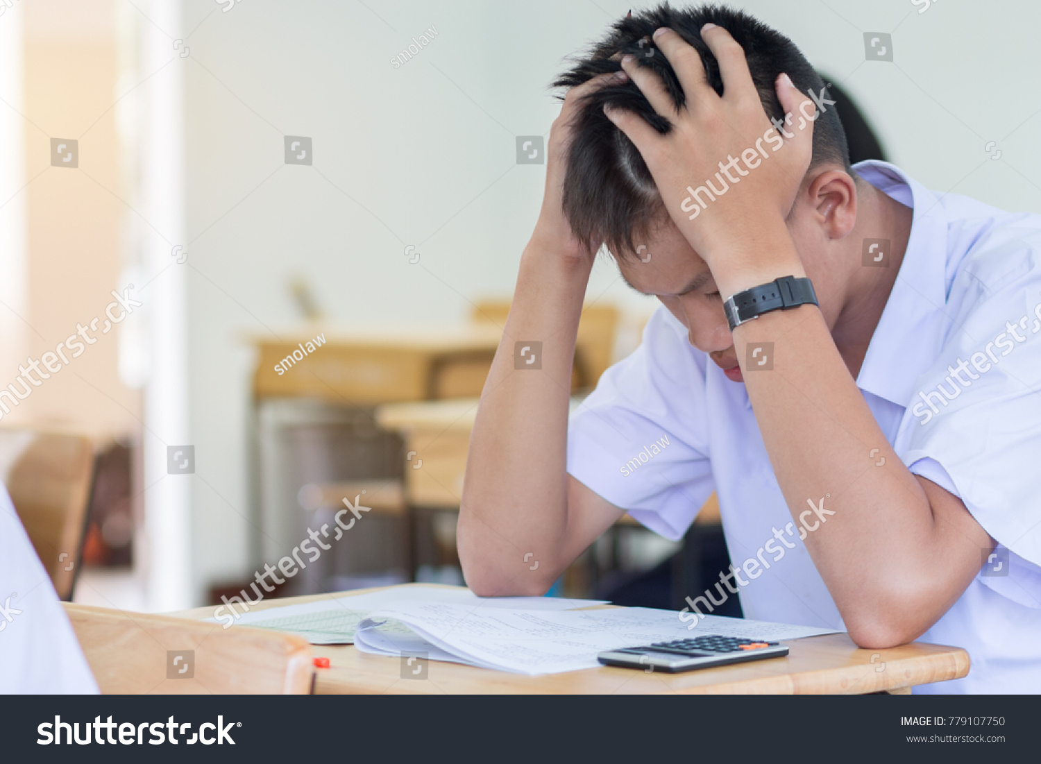 Asian boy student studying stressed headaches for test or exams in classroom, learning lessons doing final exam at high school with Thailand uniform in class room. Education system concept. #779107750