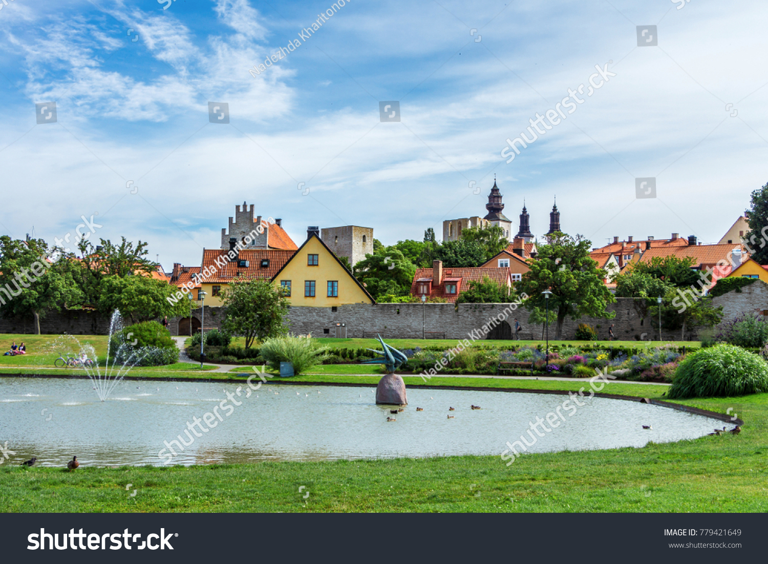 Park Almedalen in Visby, the main city on island Gotland, Sweden. The best-preserved historical medieval city in Scandinavia. Beautiful view with color old buildings, lake, resting or relaxing people. #779421649