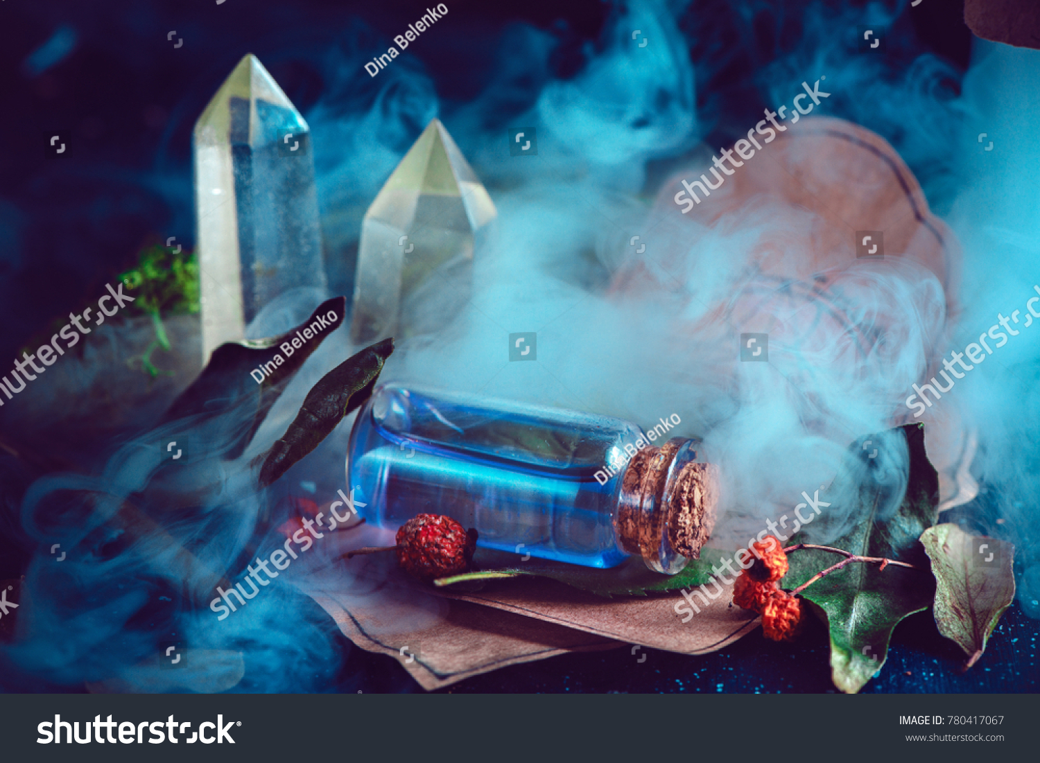Magical still life with spells, herbs, potion ingredients and a glass bottle with mystic liquid on a dark background. Modern witchcraft concept with copy space. #780417067