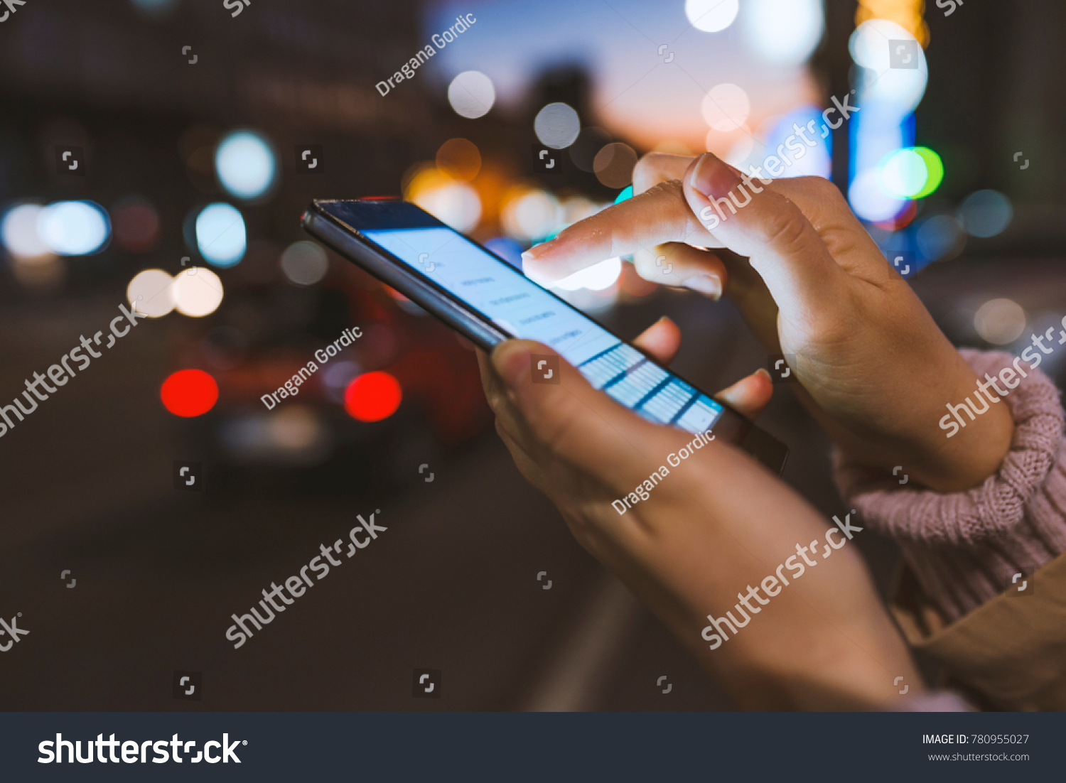 Girl pointing finger on screen smartphone on background illumination bokeh color light in night atmospheric city, using in hands texting mobile phone. Using cellphone at night #780955027