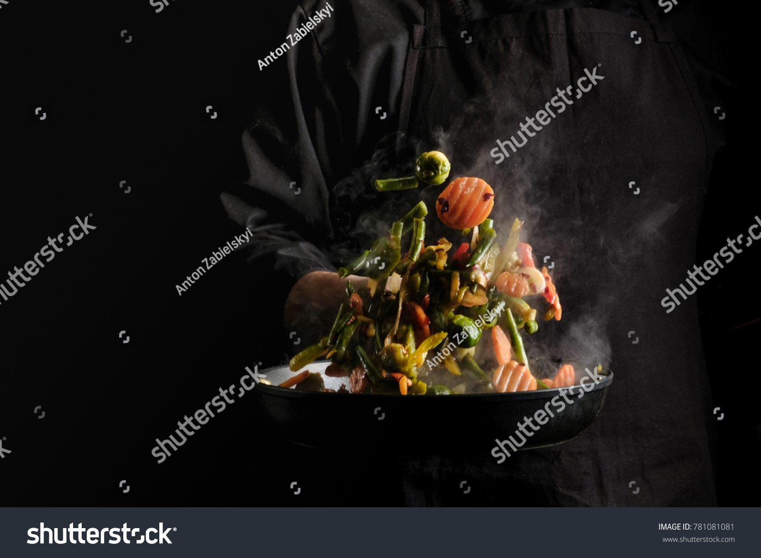 Chef cooking vegetables on a pan. Black background for copy text. #781081081