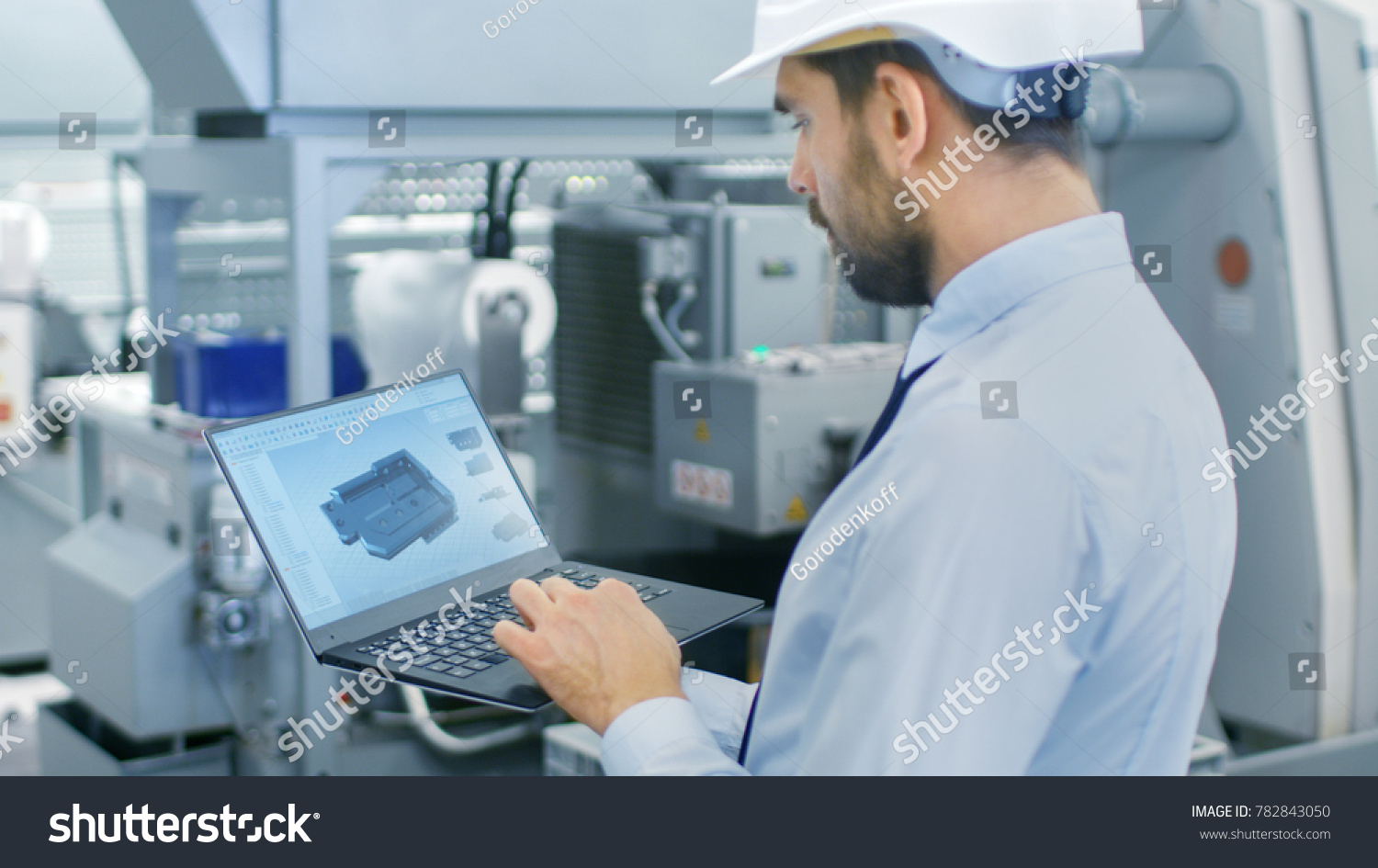 Chief Engineer in the Hard Hat Holds Laptop with 3D Component Model on it's Screen. In the Background Modern Factory Equipment. #782843050