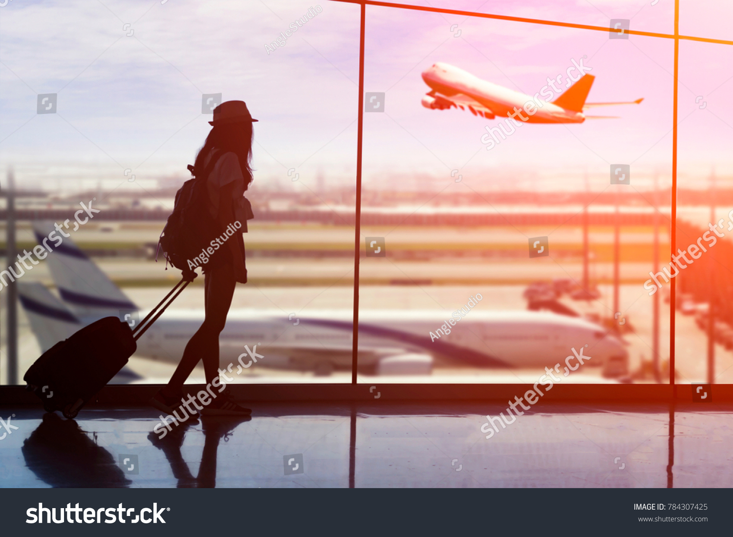 Young woman is standing near window at the airport and watching plane before departure. She is standing and carrying luggage.Travel Concept . #784307425