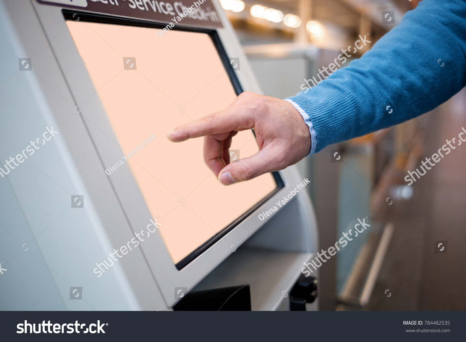 Confirm flight details. Close-up of male hands is using self-service check-in kiosk while standing at international airport building. He is registering on his airplane #784482535