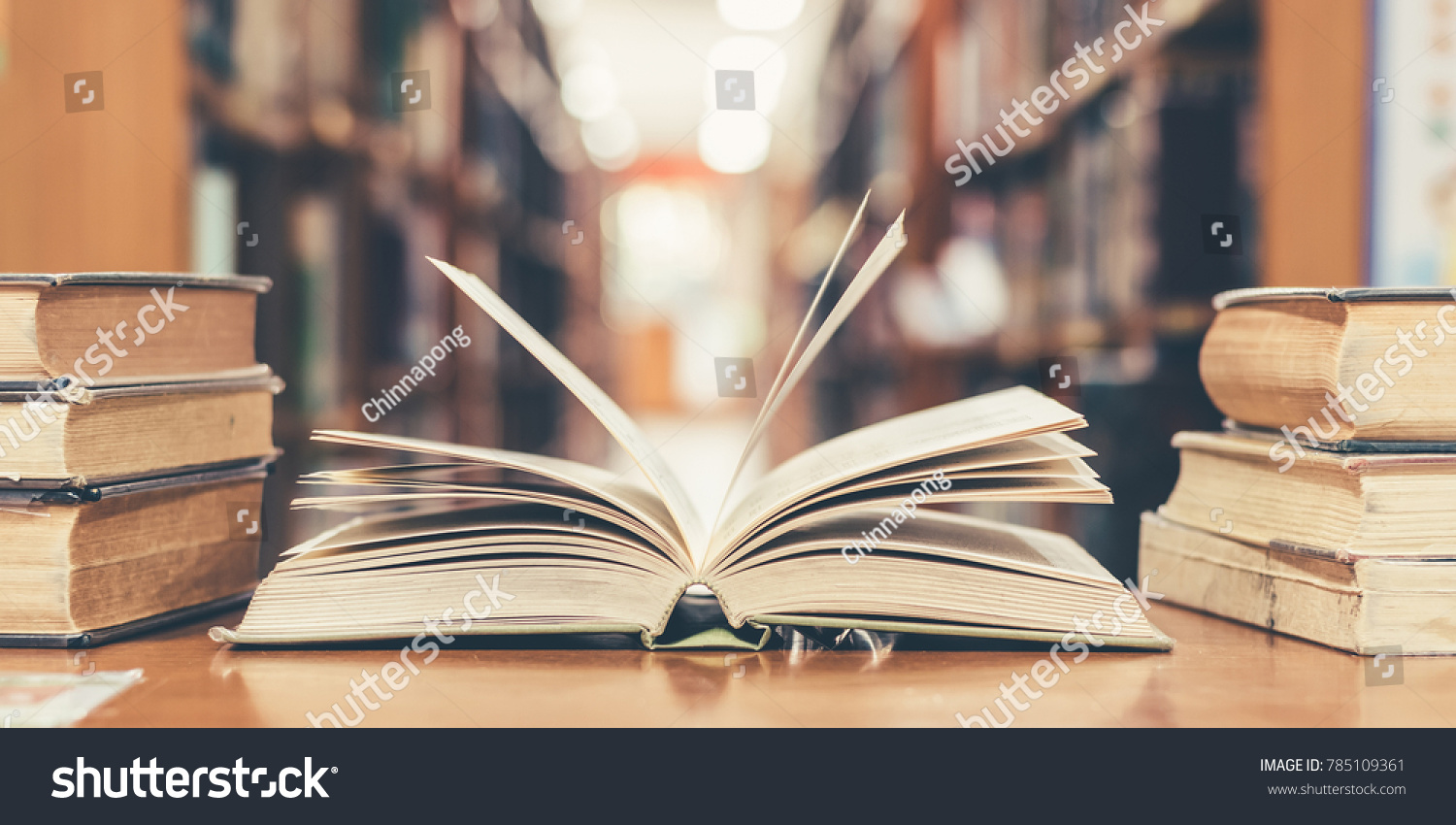 Book in library with old open textbook, stack piles of literature text archive on reading desk, and aisle of bookshelves in school study class room background for academic education learning concept #785109361