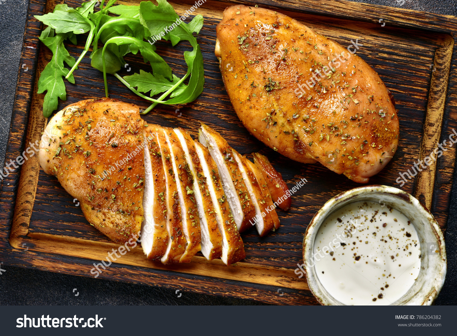 Grilled chicken breast in a sweet and sour marinade with yogurt sauce on a wooden cutting board.Top view. #786204382