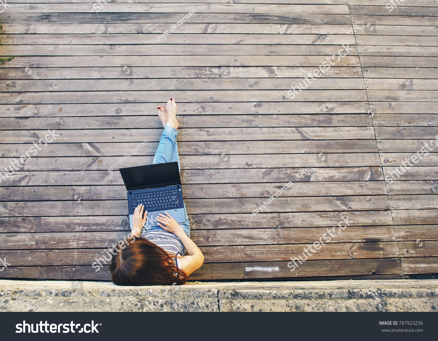 Portrait of a happy young woman sitting on the city wooden surface and using laptop computer outdoors #787923256