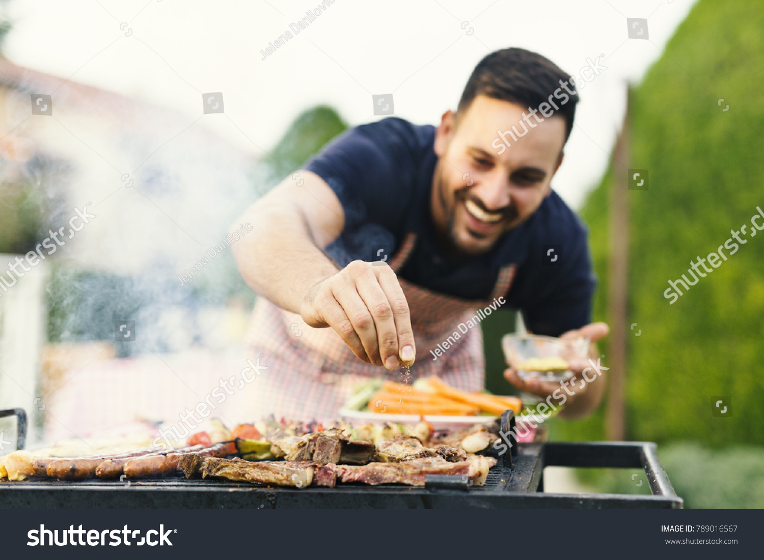 Smiling man seasoning meat on the grill #789016567