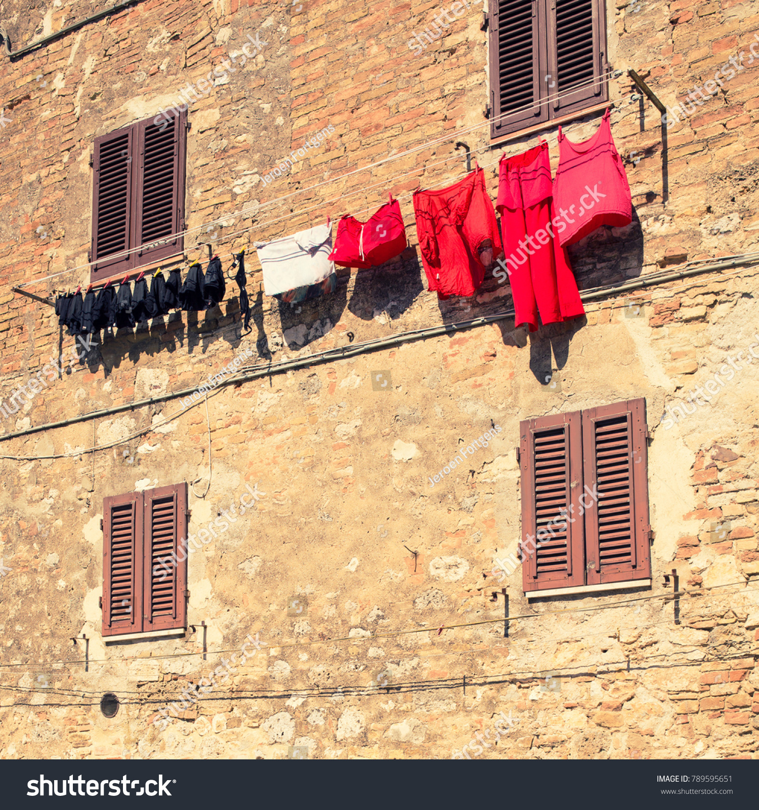 Laundry, sorted by color drying in the sun against an old brick wall and closed shutters. #789595651