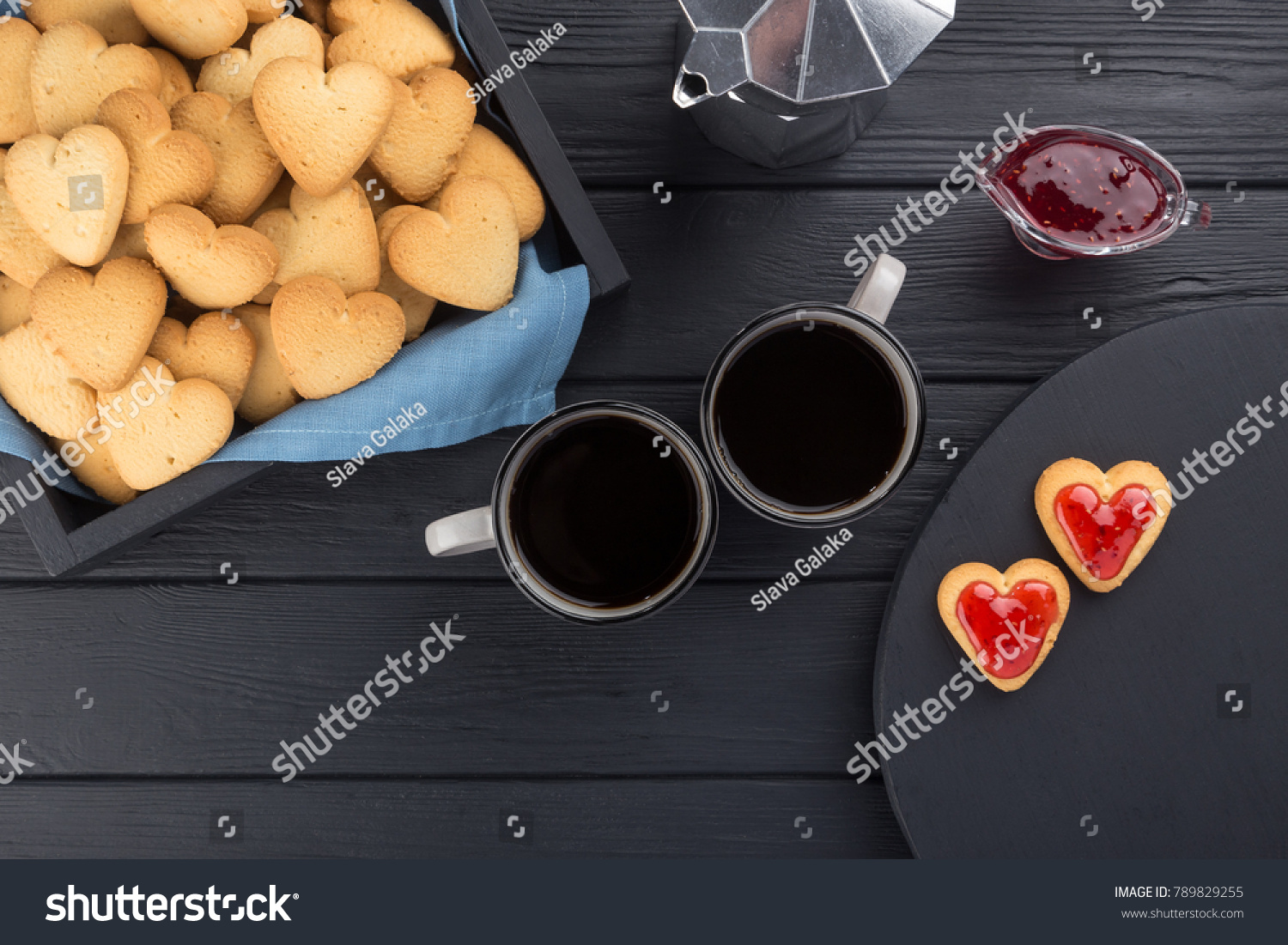 Heart shaped cookies decorated for Valentine's Day. Free space for text. Box with heart shaped cookies with coffee, coffee pot, jam on a black wooden table. Two heart shaped cookies with jam.  #789829255