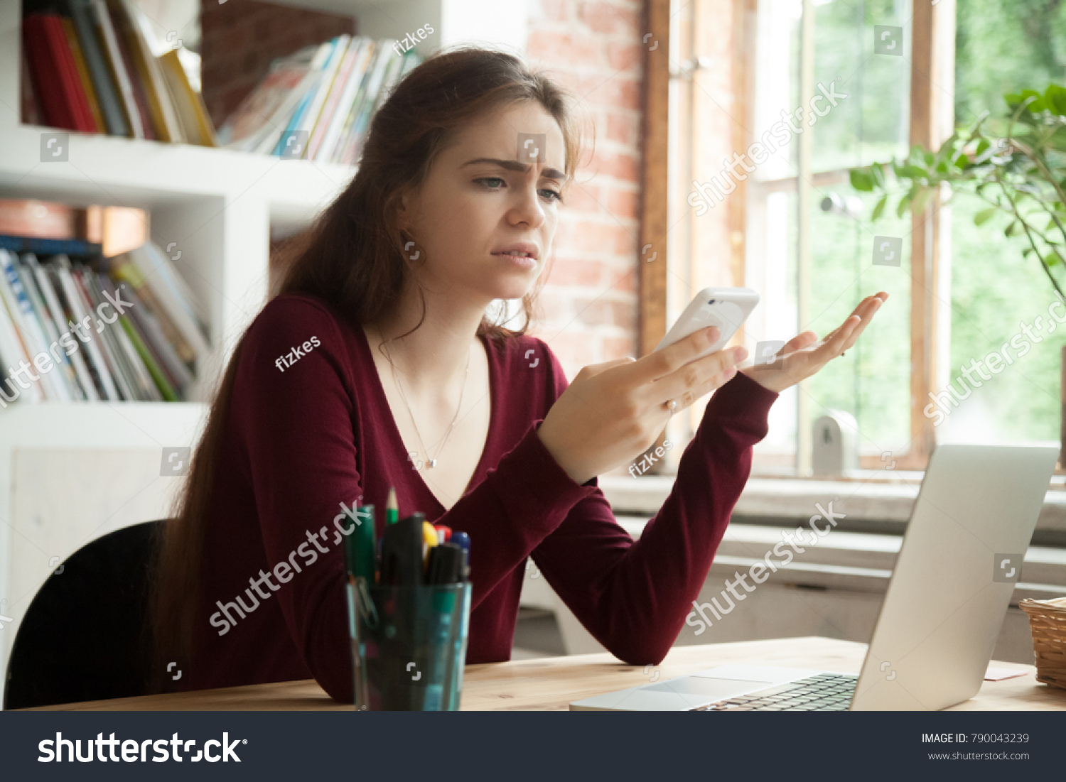 Frustrated woman having problem with not working smart phone sitting at home office desk, indignant confused businesswoman annoyed with discharged or broken cell, received bad news in mobile message #790043239