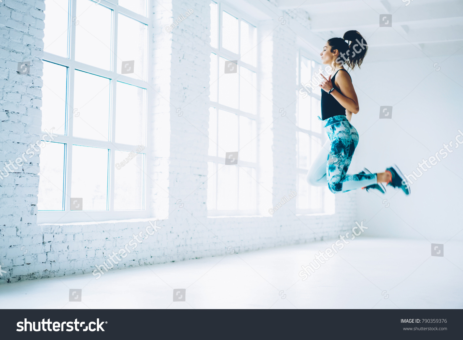 Young female in tracksuit jumping doing aerobics cardio exercises for losing weight and training strength,sportswoman doing leaps burning calories on pilates workout enjoying active lifestyle #790359376