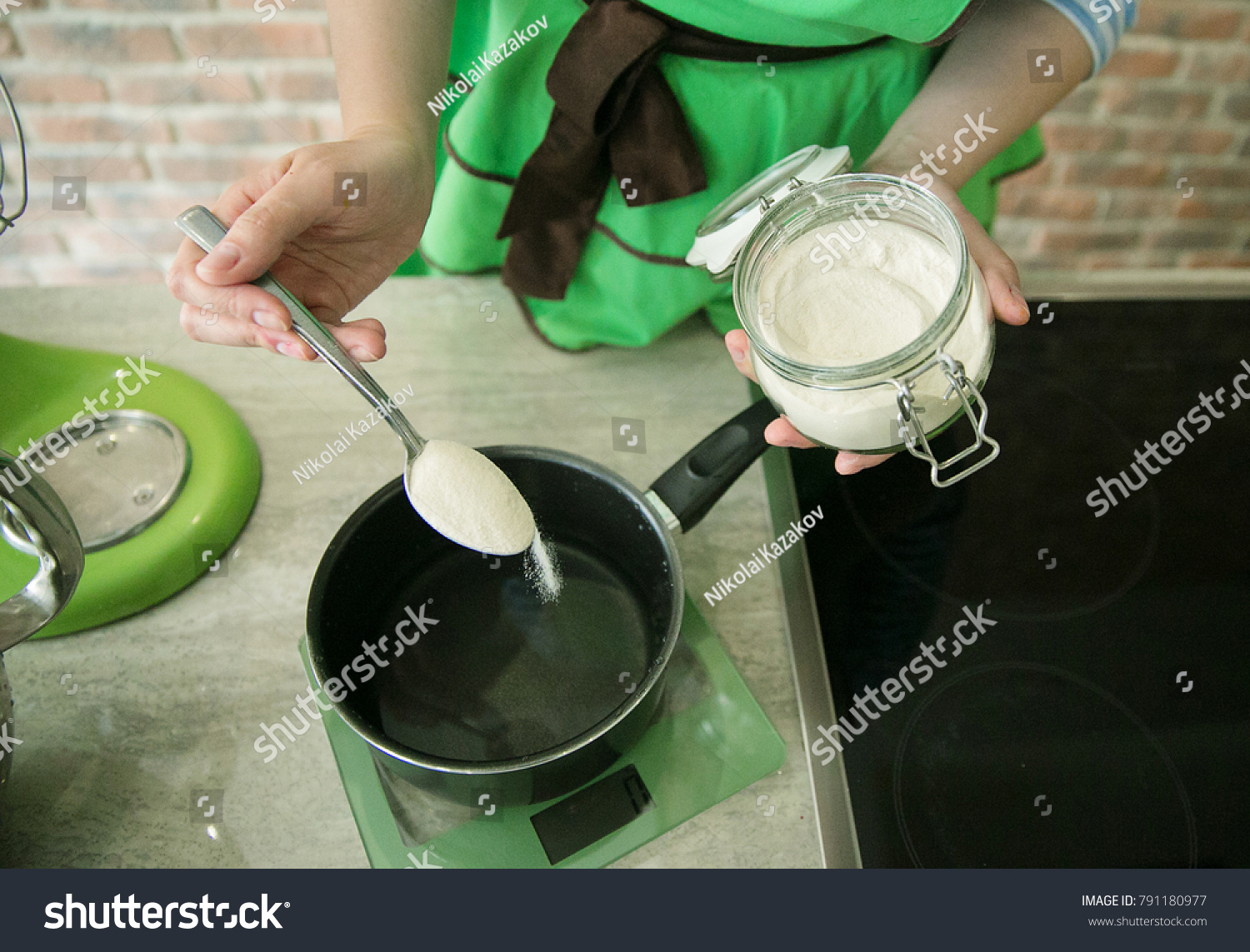 A confectioner in a green apron spoon pours agar-agar into a steel bowl with sugar syrup on the electric stove. cooking marshmallows.Homemade sweet. Homemade marshmallow dessert.  #791180977