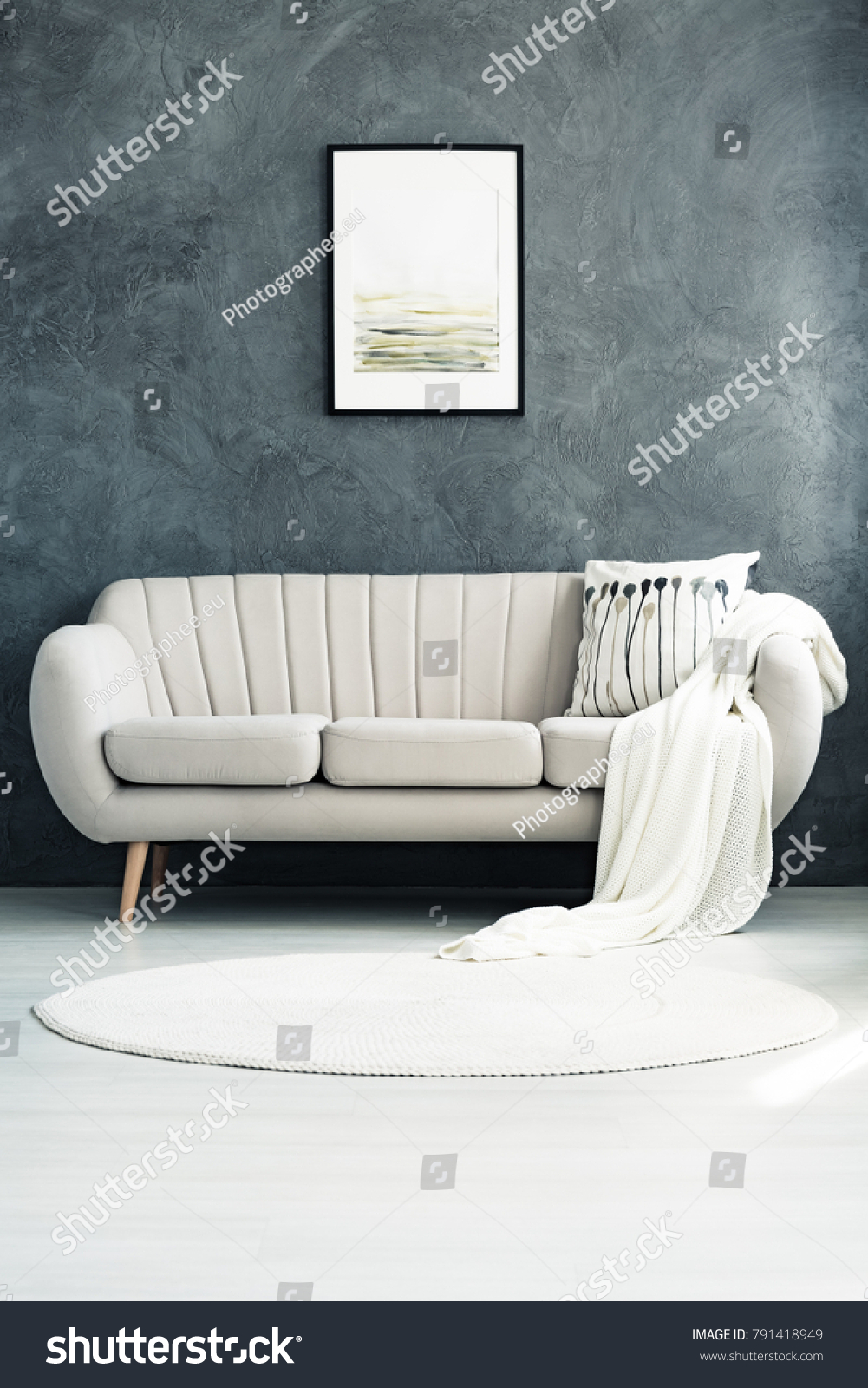 White circular rug lying in front of a comfortable beige sofa with a pillow and a blanket #791418949