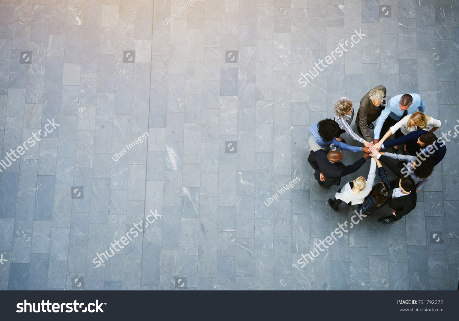 High angle view of a team of united businesspeople standing with their hands together in a huddle in the lobby of a modern office building #791792272