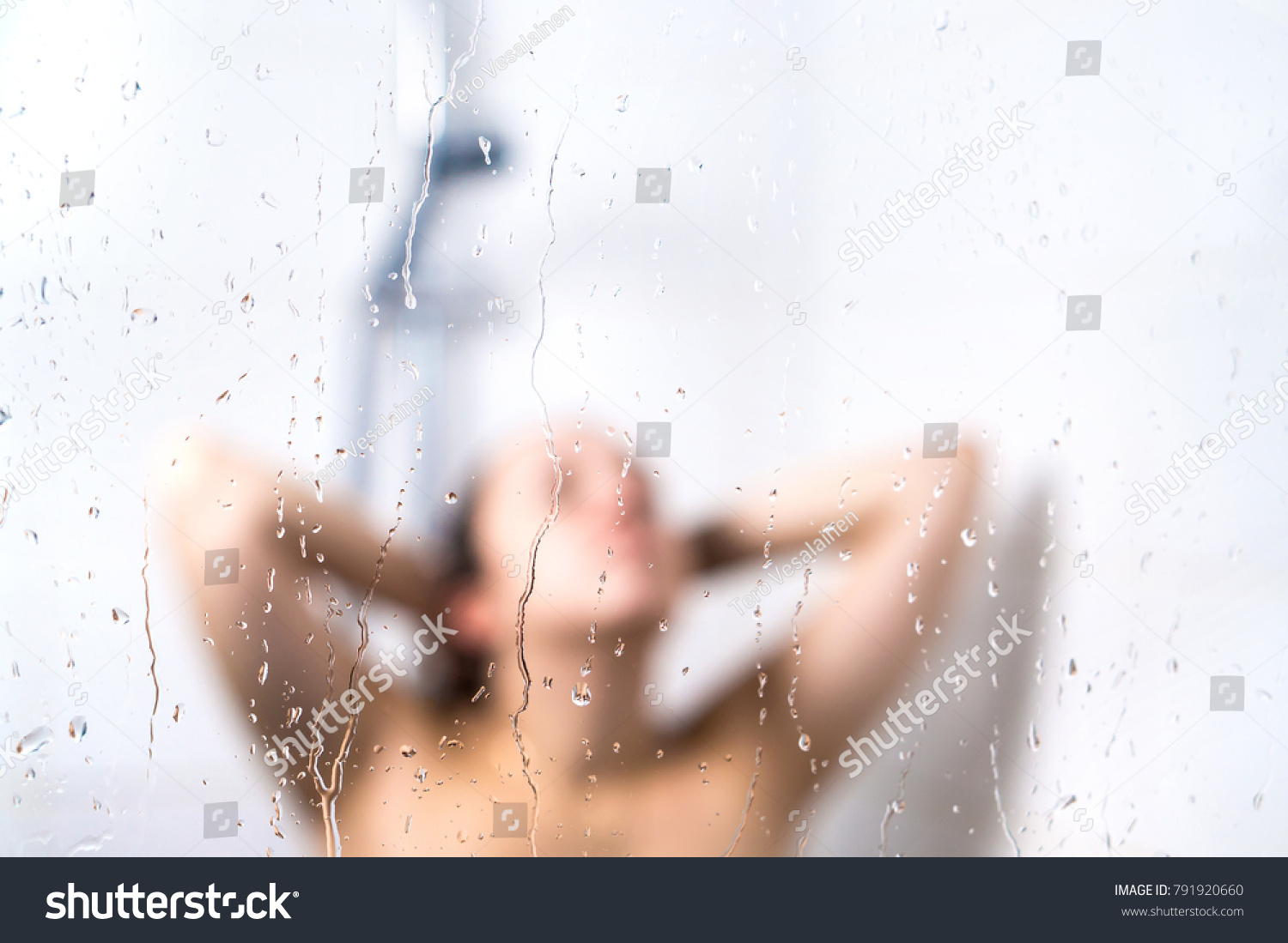 Young beautiful woman in shower. Behind wet glass window with water drops. Focus on droplets. Girl bathing, washing hair and taking fresh bath. #791920660