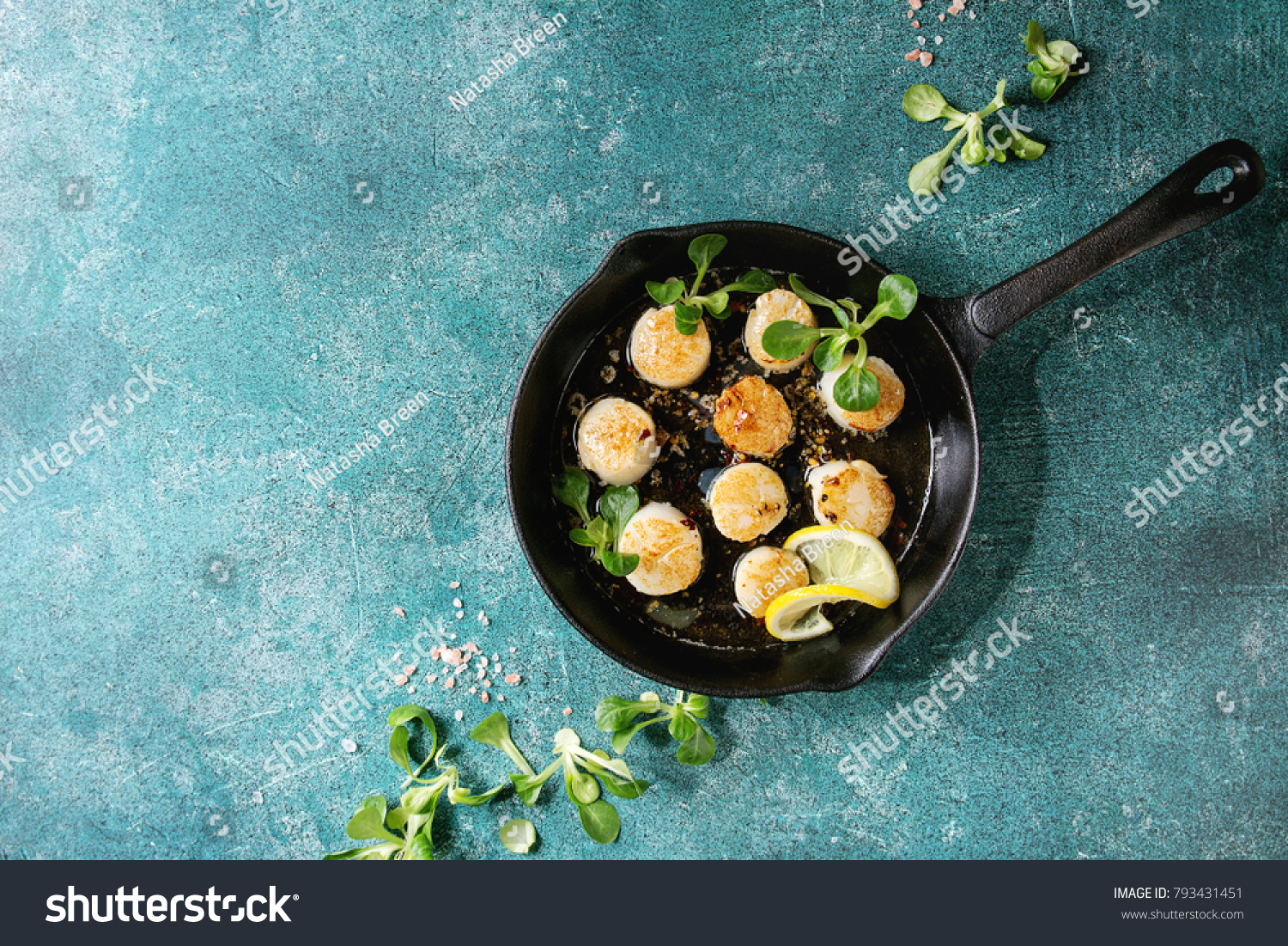 Fried scallops with butter lemon spicy sauce in cast-iron pan served with green salad over turquoise texture background. Top view, copy space #793431451