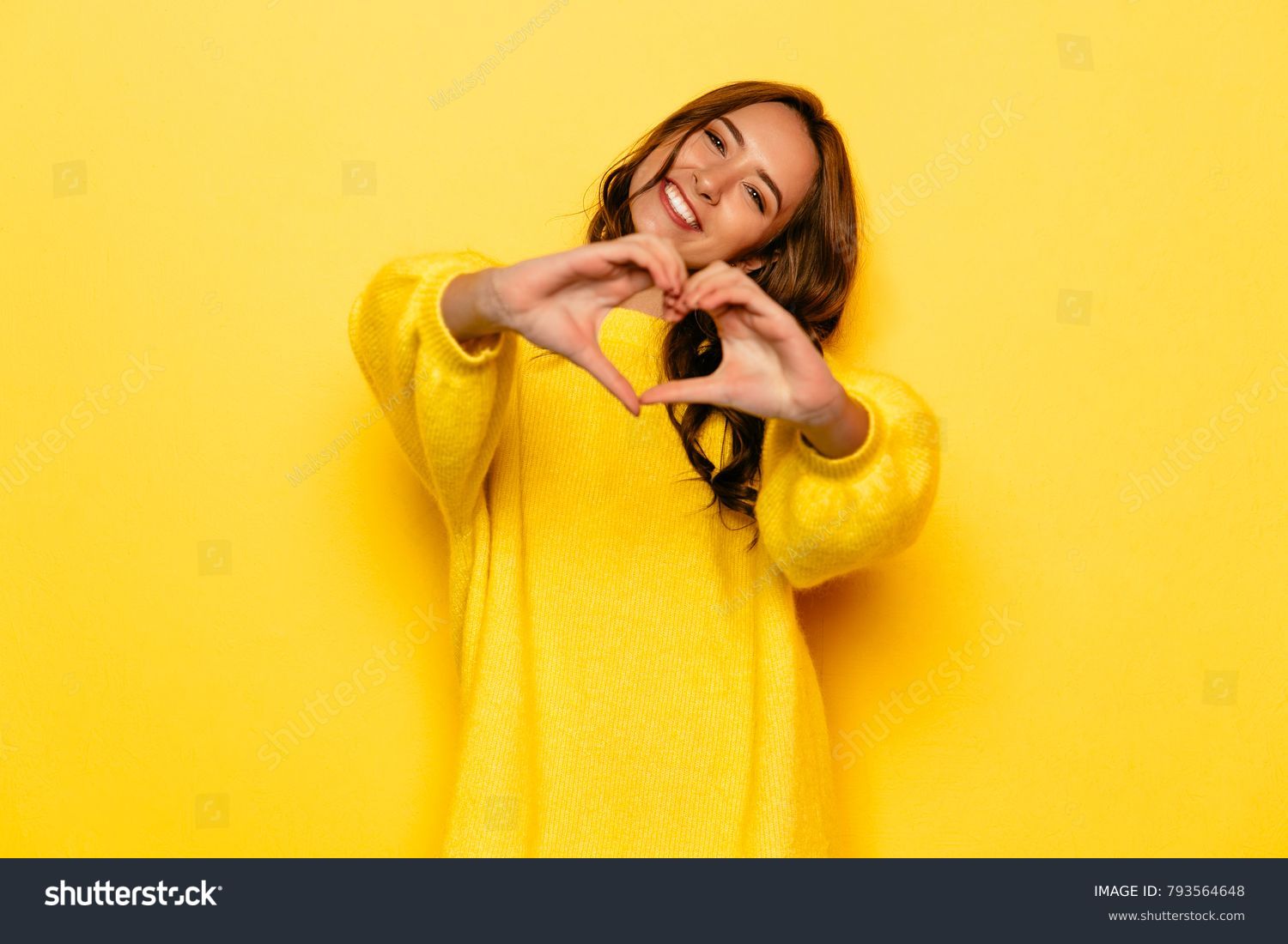 Smiling young girl in yellow sweater showing heart with two hands, love sign. Isolated over yellow background. #793564648