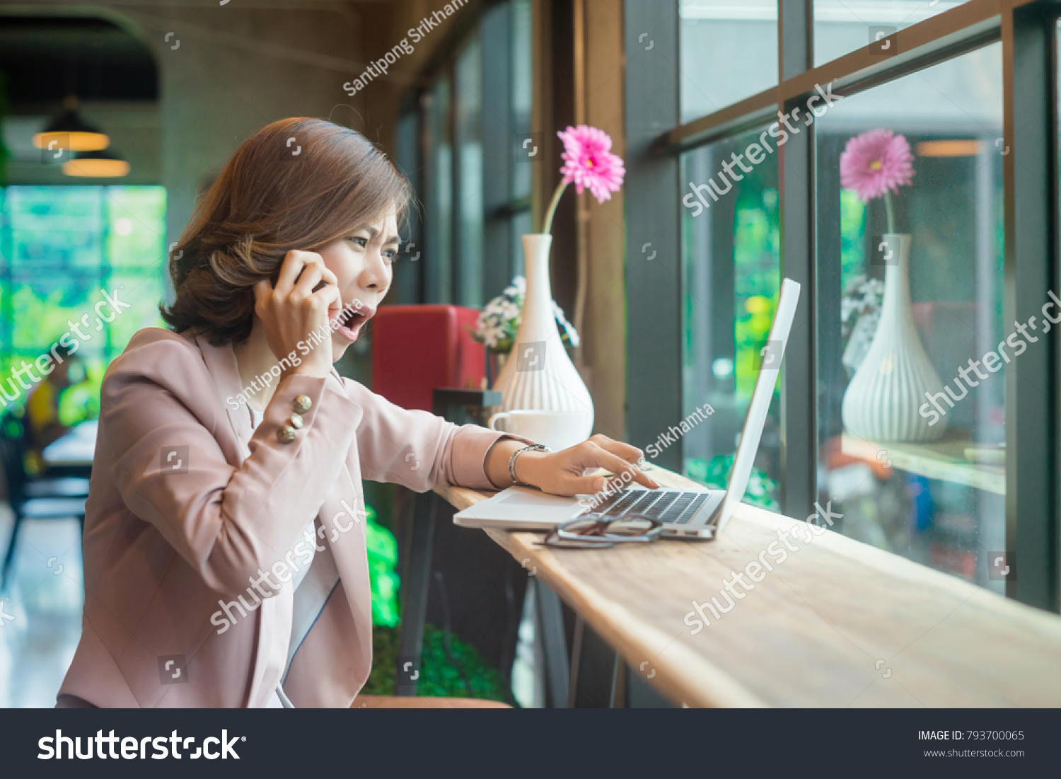 Young asian business woman talking on the cellphone with stressed face or be unhappy with the result of something on the laptop. #793700065