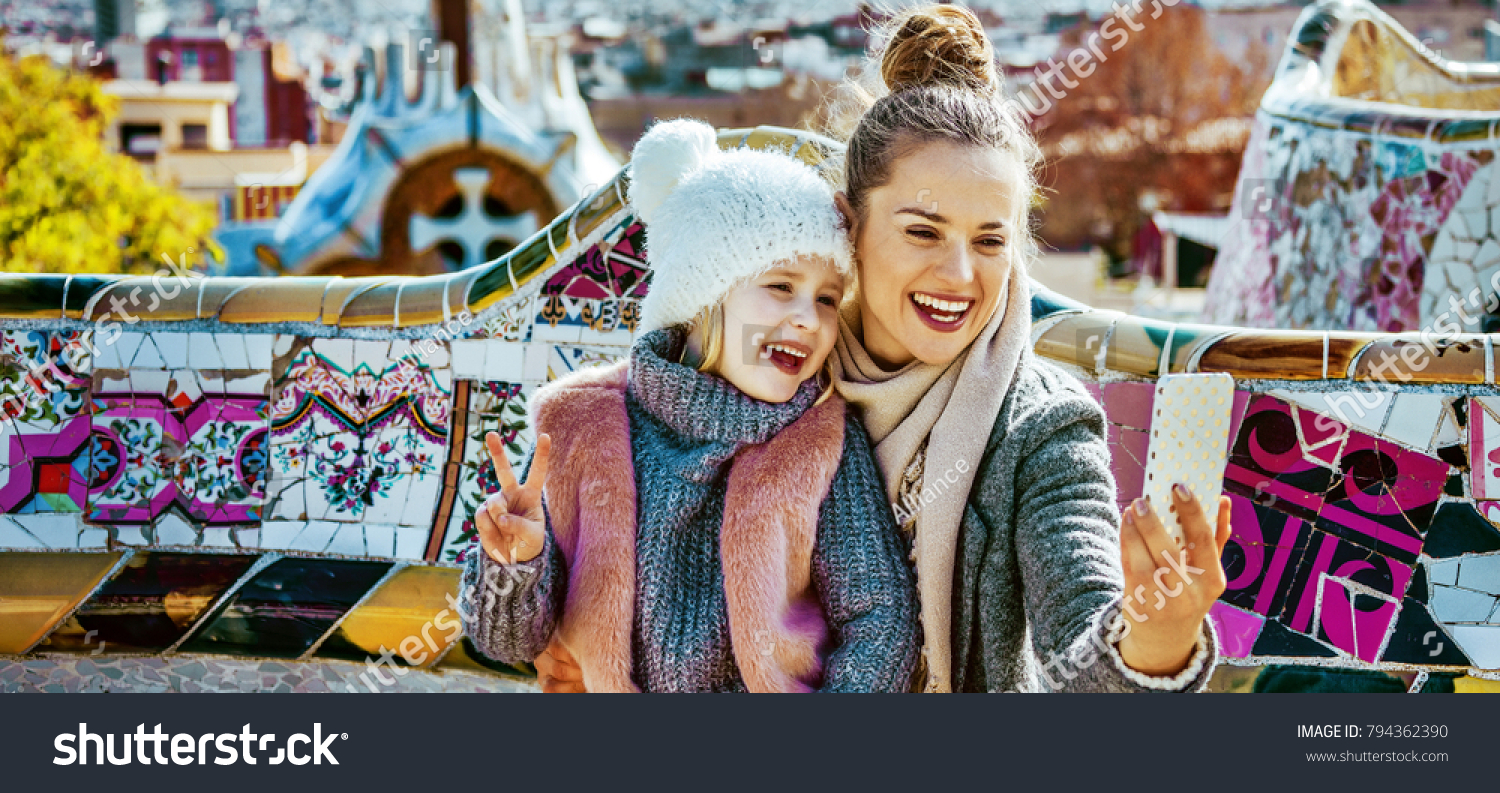 Barcelona signature style. Portrait of smiling trendy mother and daughter tourists in Barcelona, Spain with smartphone taking selfie while sitting on a bench #794362390