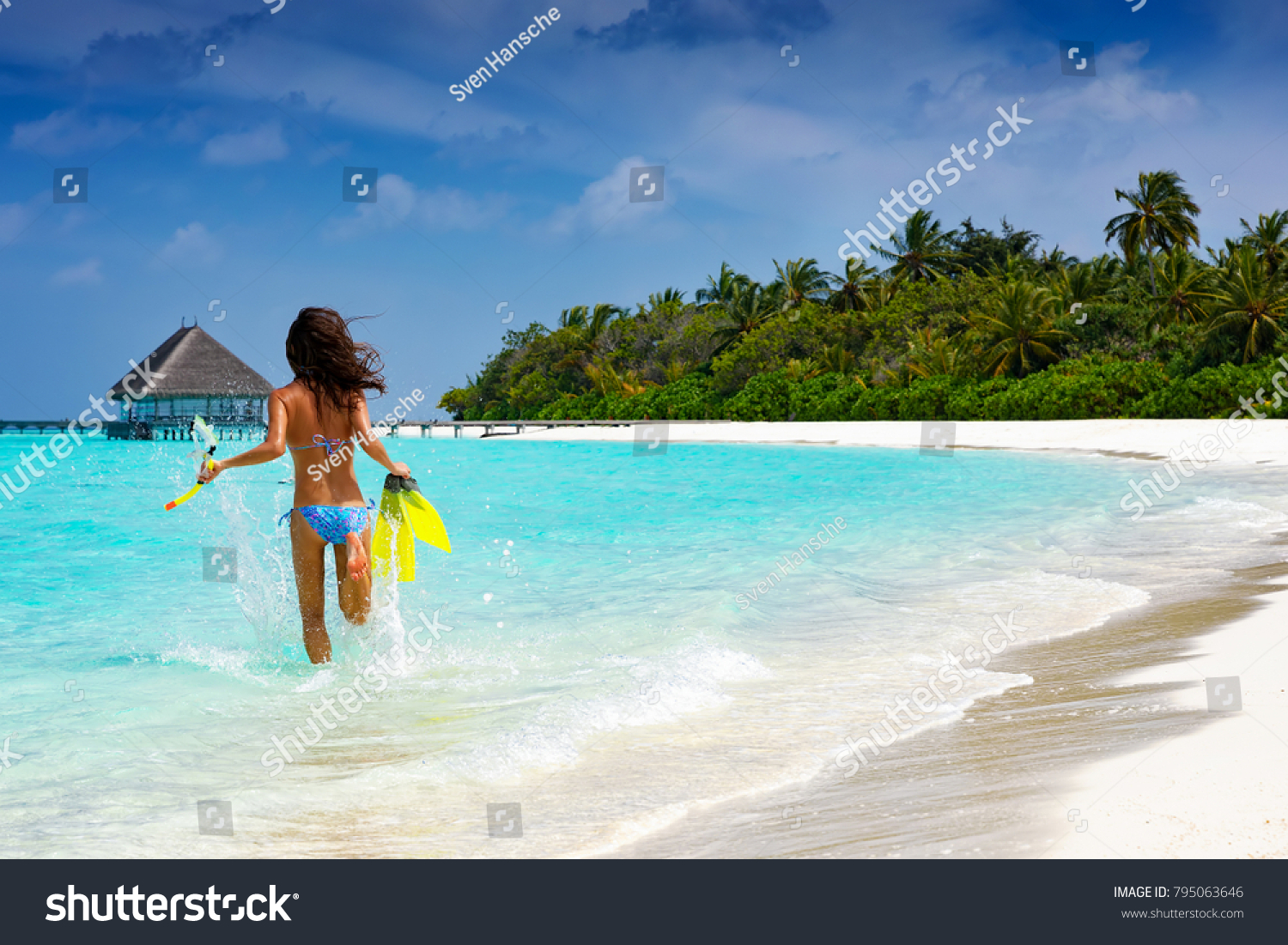 Woman with snorkeling gear running into the turquoise, tropical waters of the Maldives #795063646