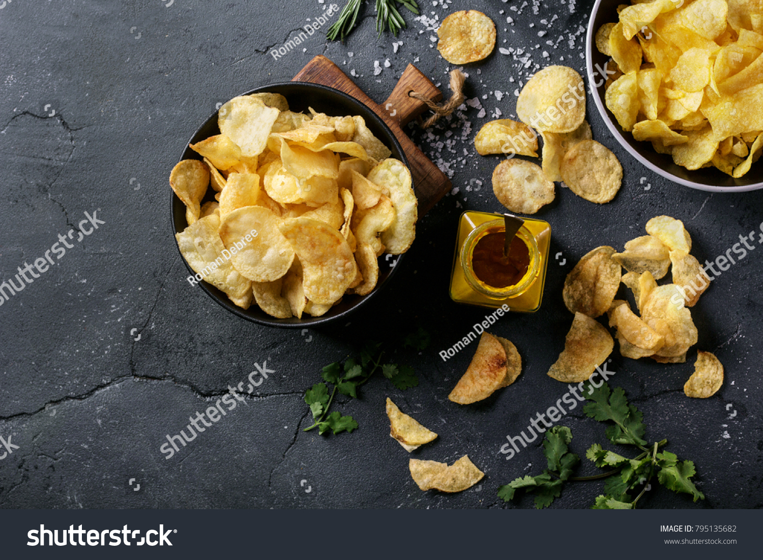 Bowl of home made potato chips served with mustard, rosemary, fleur de sel salt on stone background. Top view. Copy space #795135682