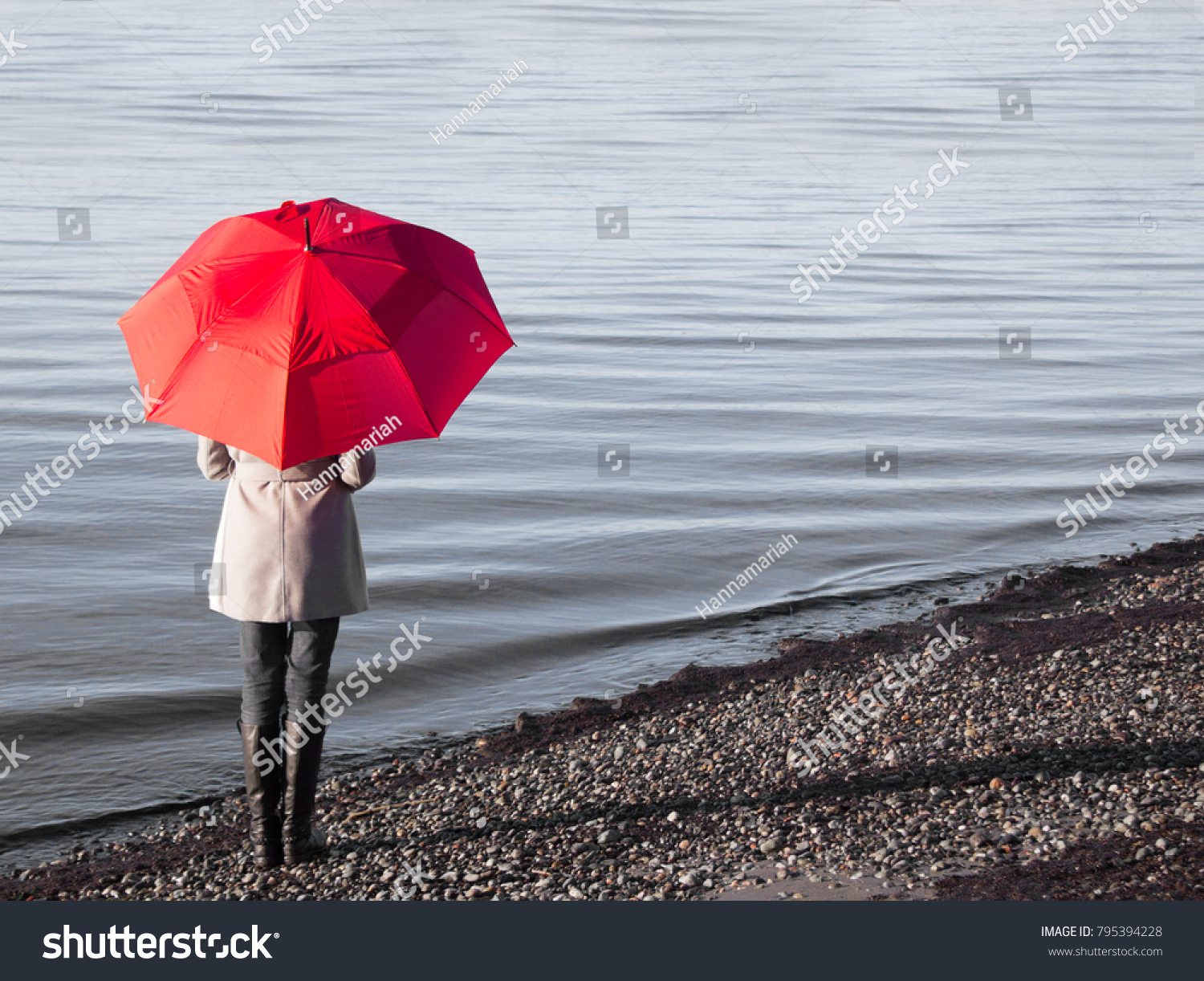 Woman holding a red umbrella walking on a rainy day at a beach.  #795394228