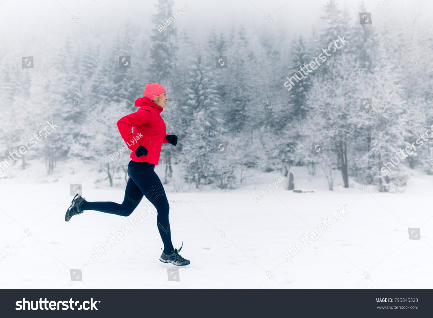 Woman running on snow in winter mountains. Sport, fitness inspiration and motivation. Young happy woman trail running in mountains on snow, winter day. Female trail runner jogging outdoors. #795845323