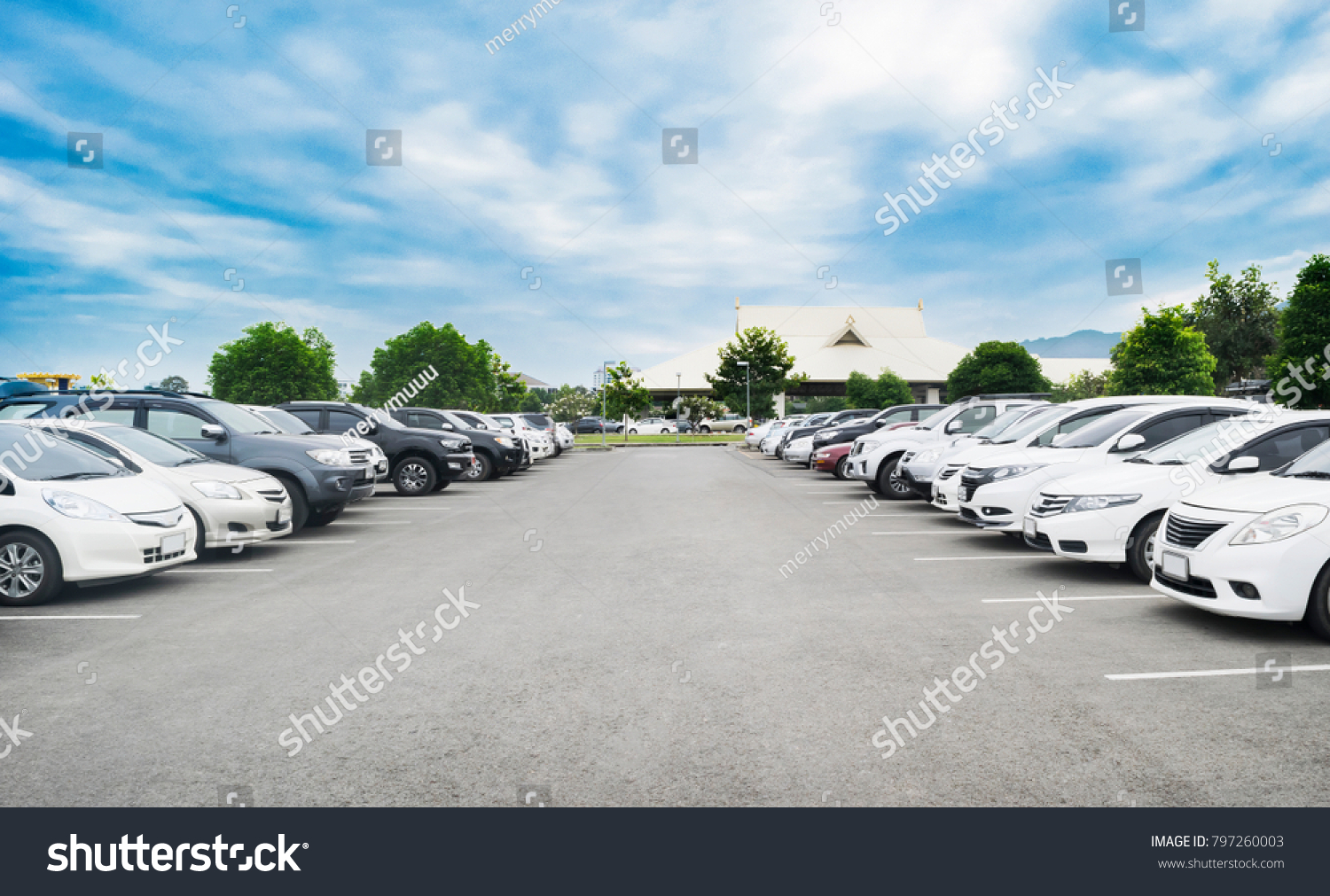 Car parking in large asphalt parking lot with trees, white cloud and blue sky background in front of hall building. Outdoor parking lot with fresh ozone and green environment concept #797260003