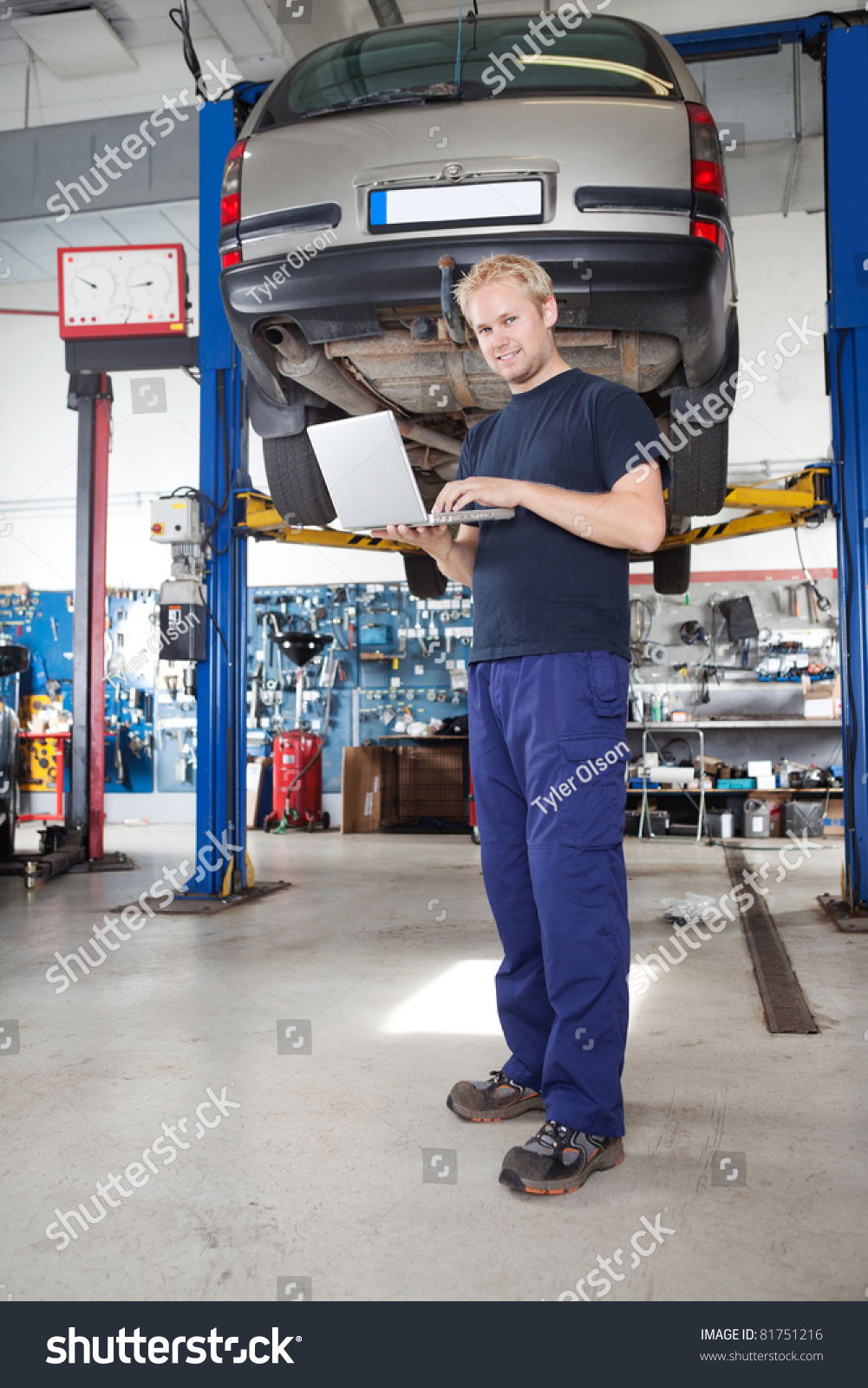 Full length portrait of smiling young mechanic using laptop in his auto repair shop #81751216