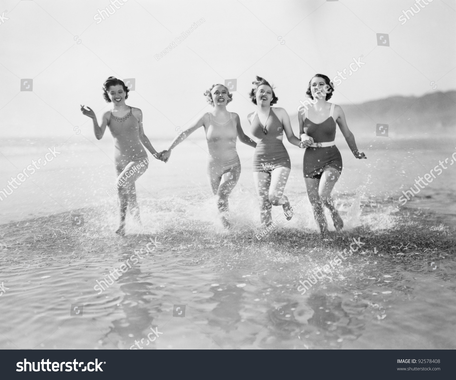 Four women running in water on the beach #92578408