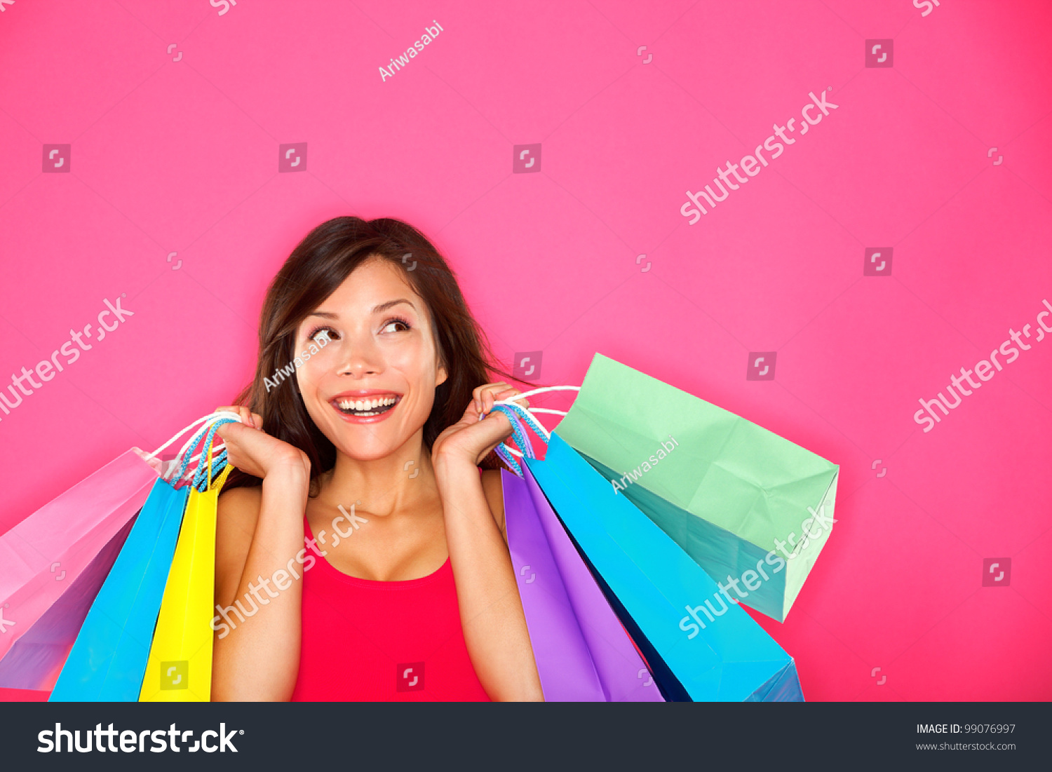 Shopping woman holding shopping bags looking up to the side on pink background at copy space. Beautiful young mixed race Caucasian / Chinese Asian shopper smiling happy. #99076997