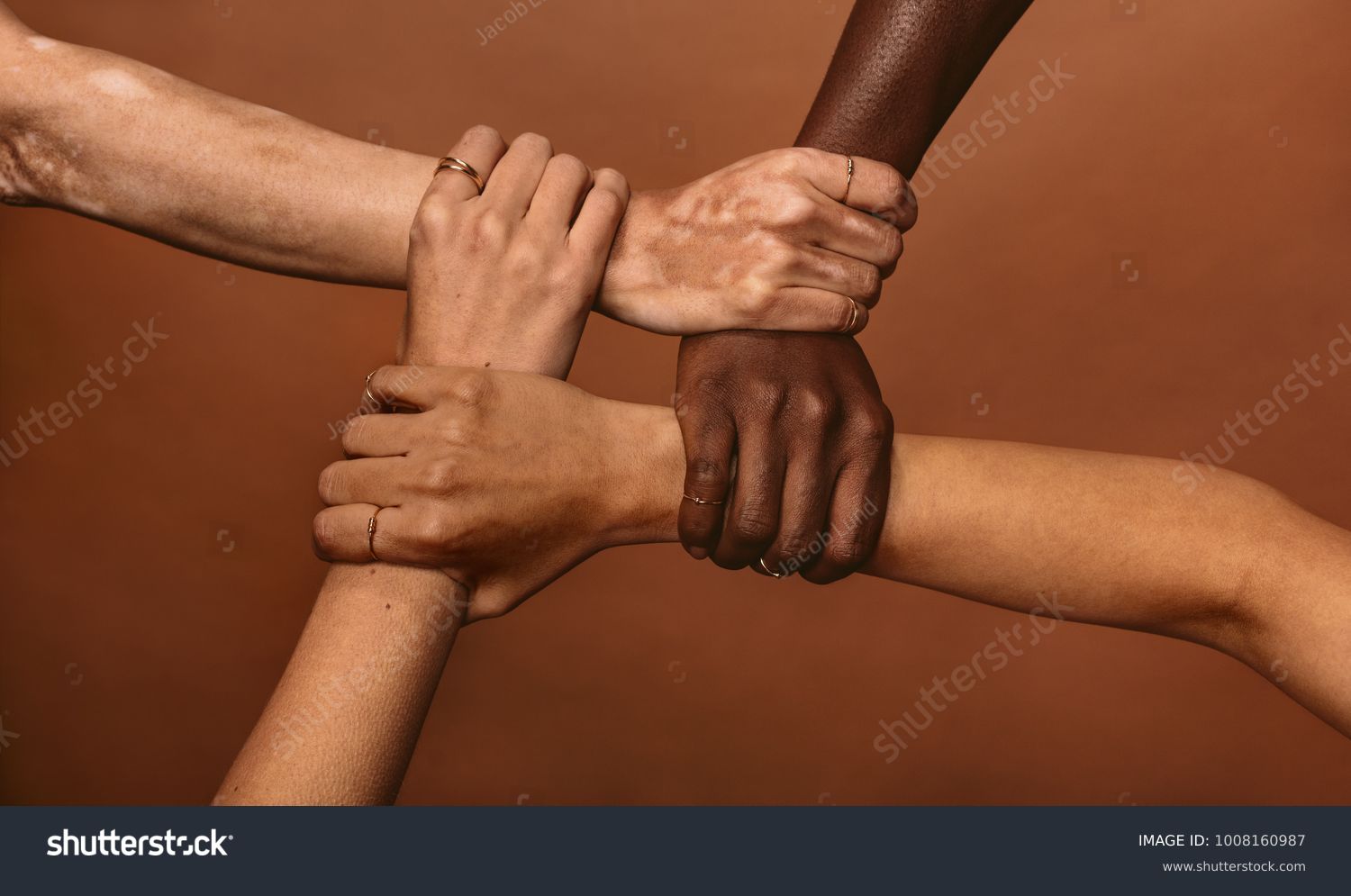 Four diverse women holding each others wrists in a circle. Top view of female hands linked in the lock against brown background. #1008160987