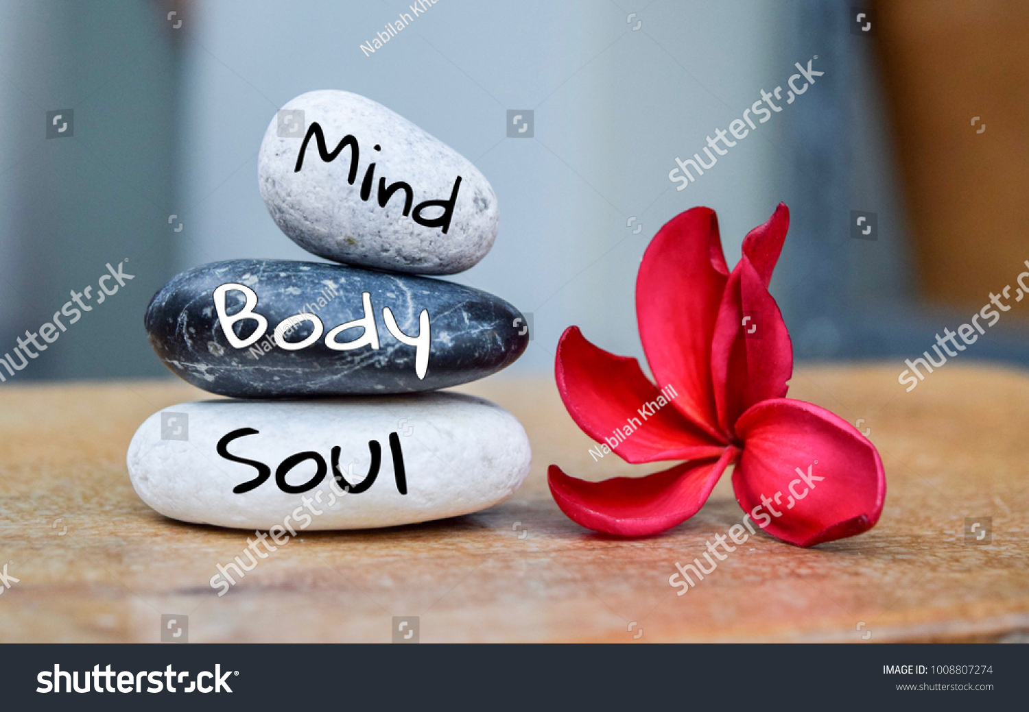 Holistic health concept of zen stones with deep red plumeria flower on blurred background. Text body mind soul. #1008807274