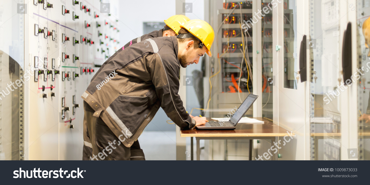 Two maintenance engineers inspect relay protection system with laptop computer. Bay control unit. Medium voltage switchgear #1009873033