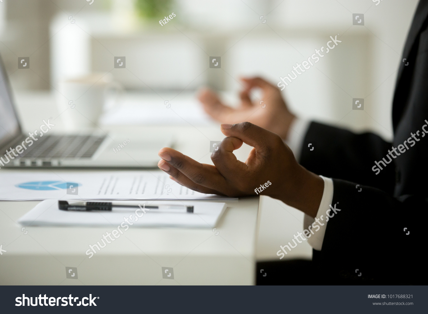 African american calm businessman relaxing meditating in office, peaceful ceo in suit practicing yoga at work, focus on black man hands in mudra, successful mindful people habits concept, close up #1017688321