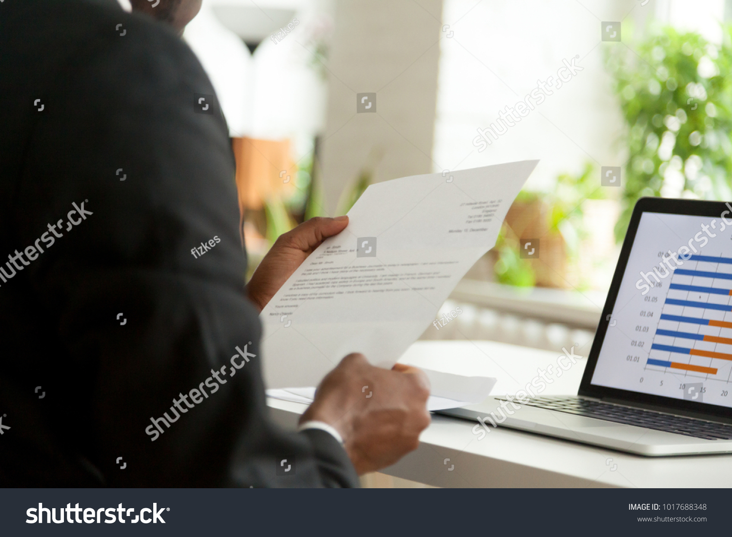 African-american hr manager or employer reading cover letter from job vacancy applicant, black businessman holding business mail checking paper correspondence at workplace, over the shoulder view #1017688348